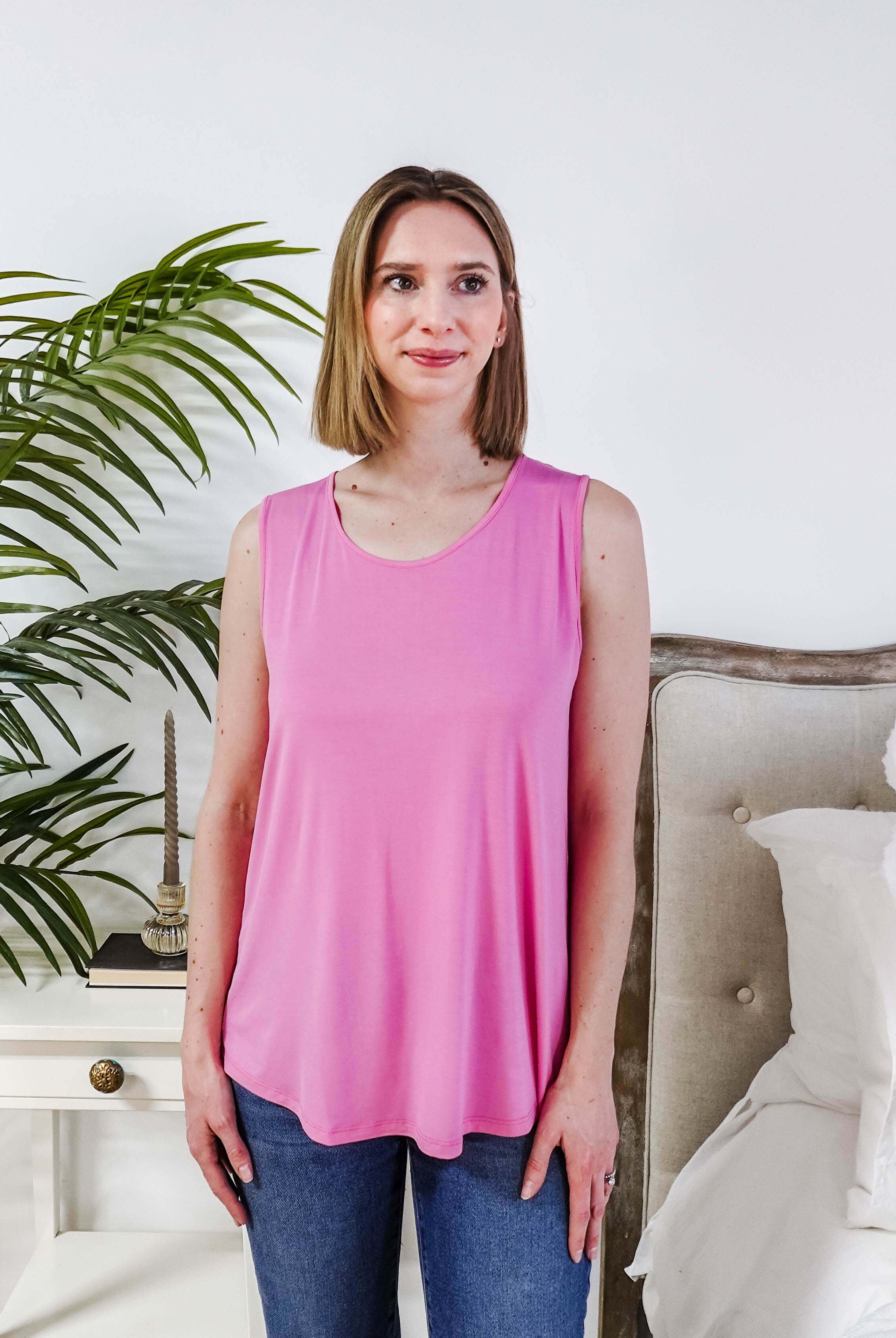 Woman wearing a Bubblegum Pink Essential Bamboo Tank Top in a stylish room setting with greenery.