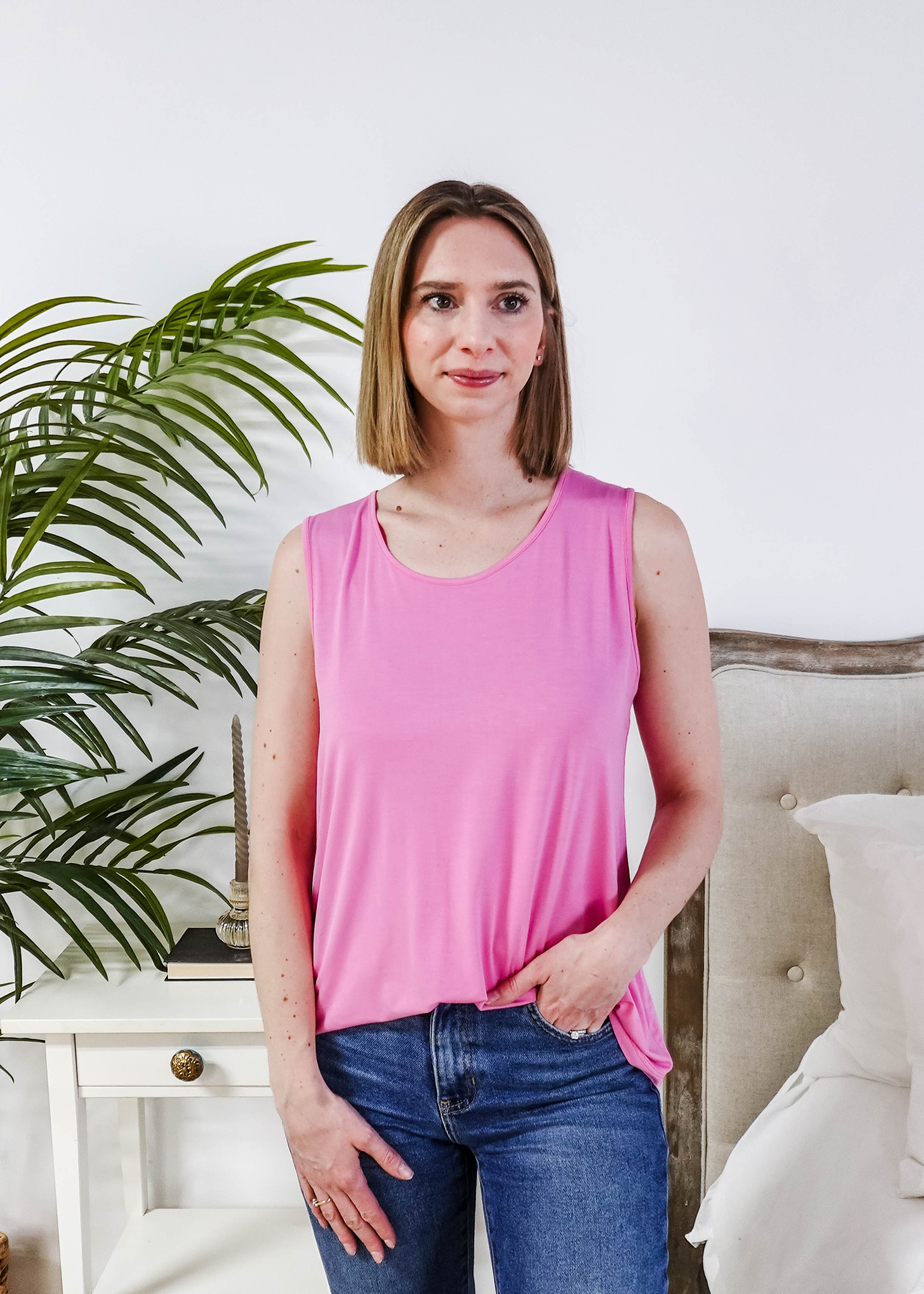 Model wearing the Bubblegum Pink Essential Bamboo Tank Top with jeans and a plant in the background.