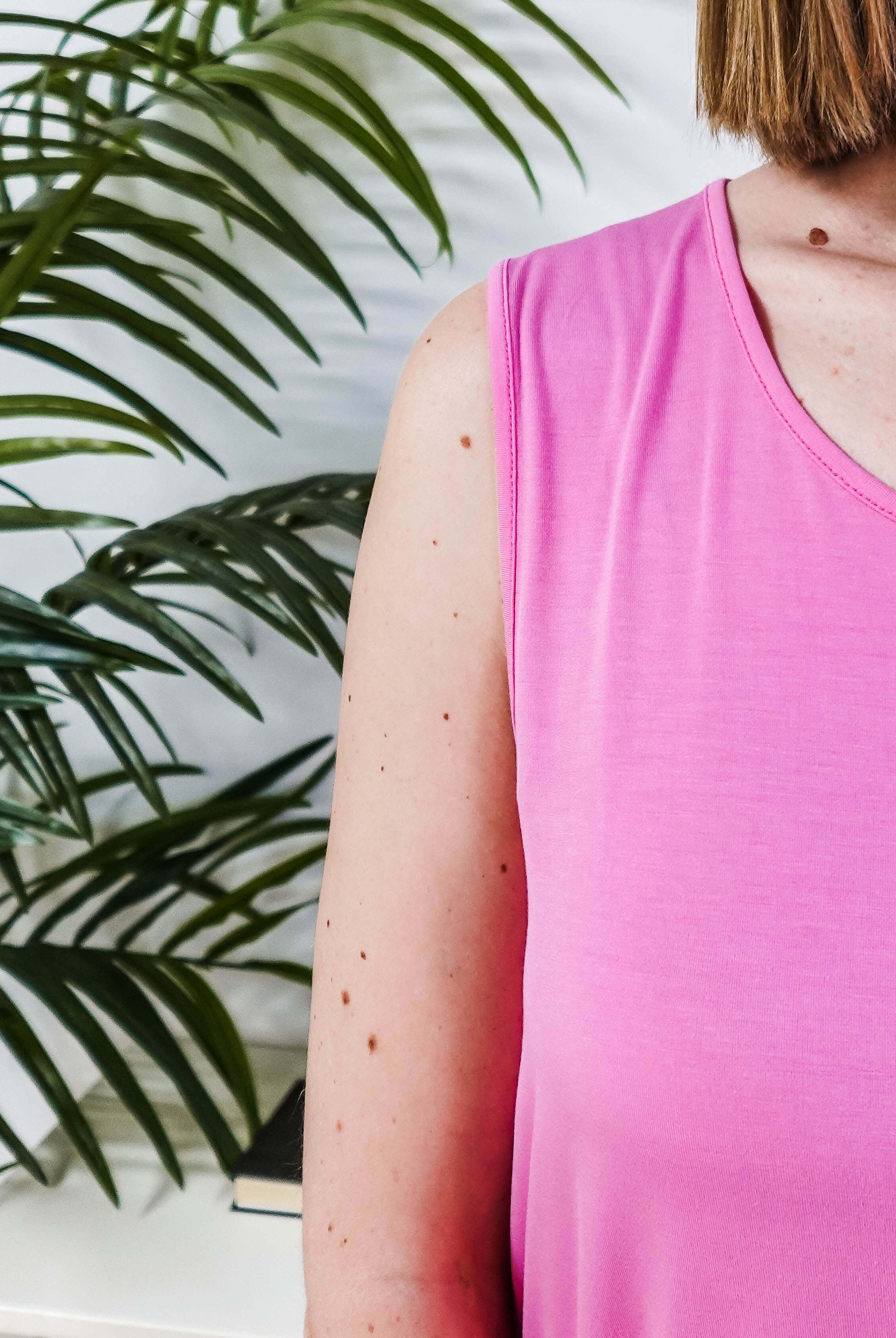 Close-up of a woman wearing the Bubblegum Pink Essential Bamboo Tank Top next to a green plant.