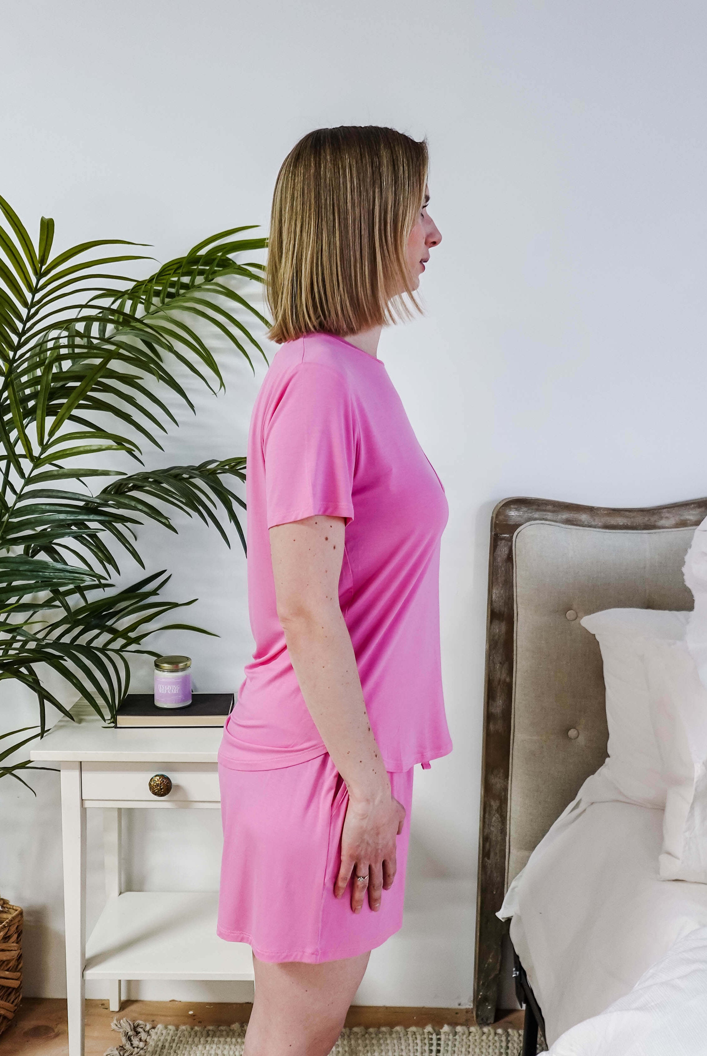 Bubblegum Pink Tee Short Bamboo Pajama Set worn by a woman standing in profile in a cozy bedroom.