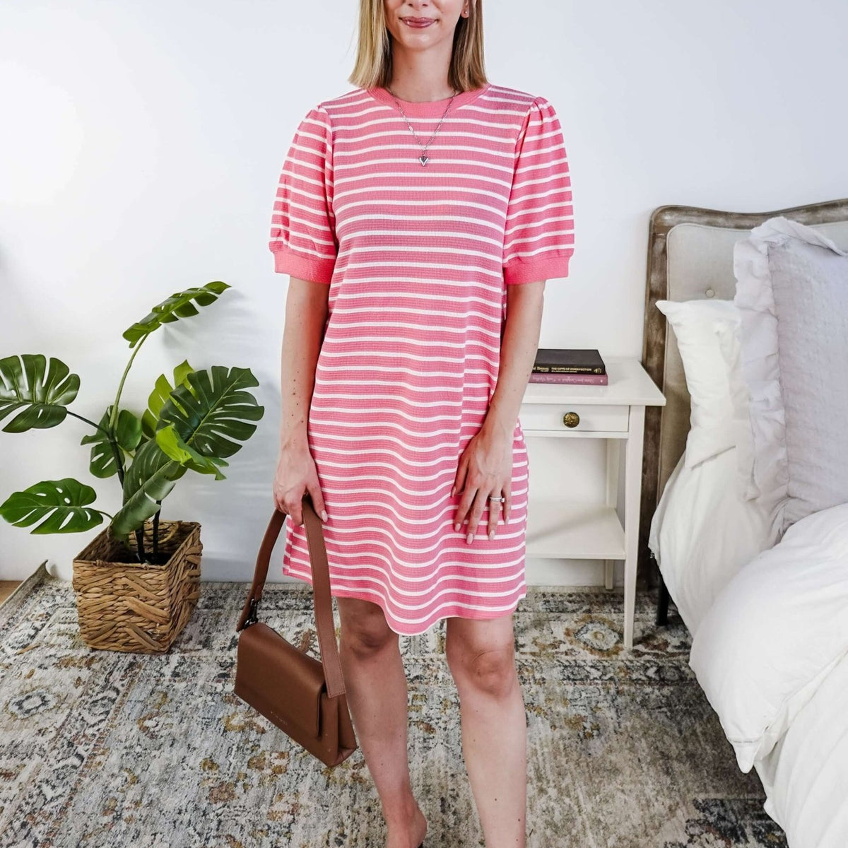 Woman wearing a pink and white striped dress with puffed sleeves in a bedroom setting.