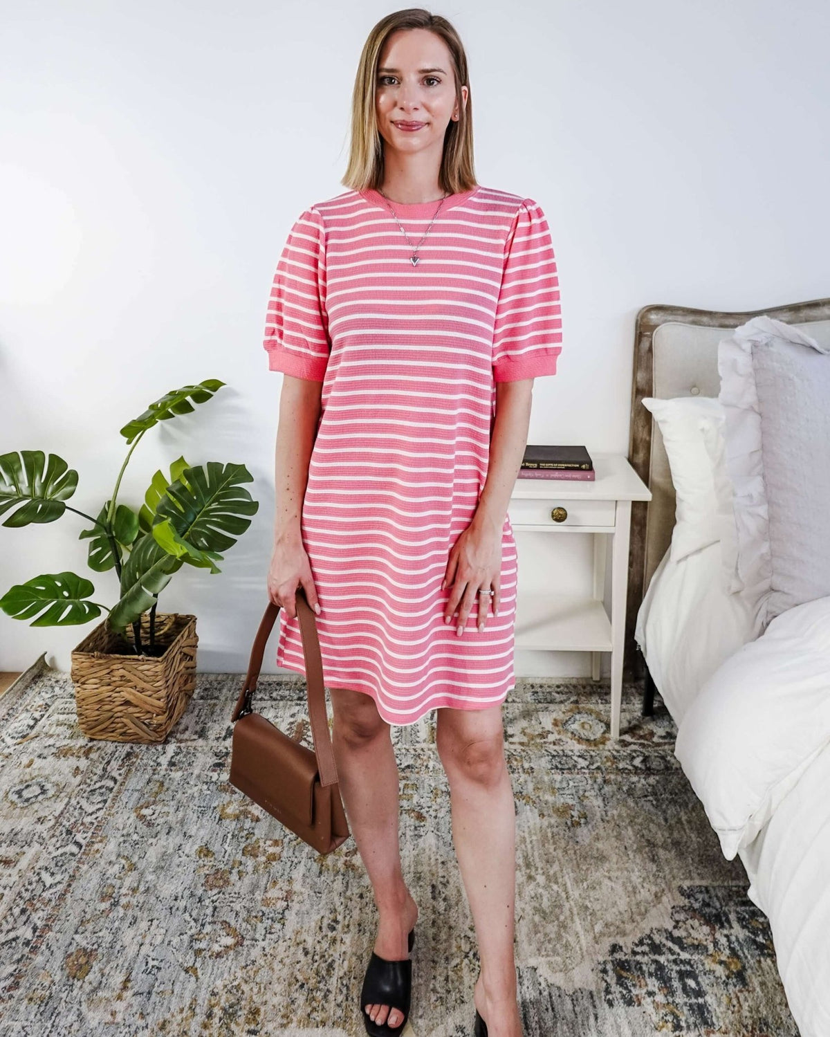 Woman wearing a pink and white striped dress with puffed sleeves in a bedroom setting.