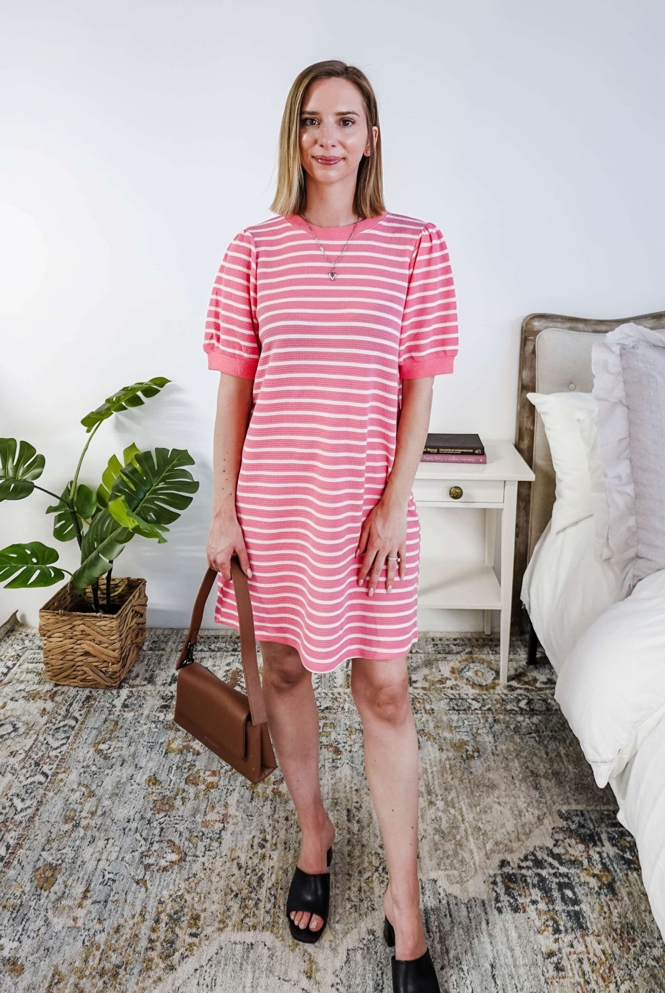 Woman wearing a pink and white striped dress with puffed sleeves in a bedroom setting.