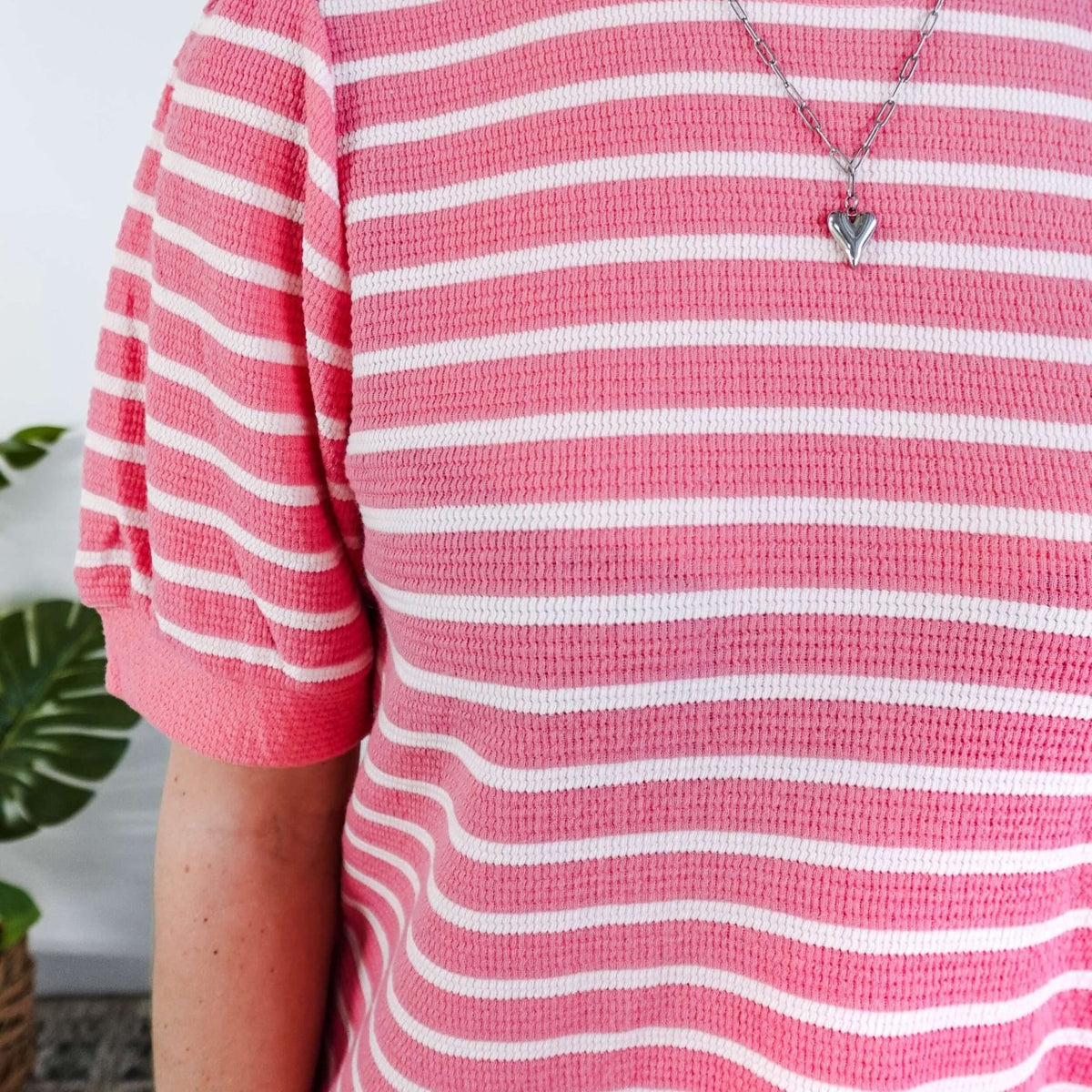 Close up of a woman wearing a pink and white striped dress with puffed sleeves in a bedroom setting.