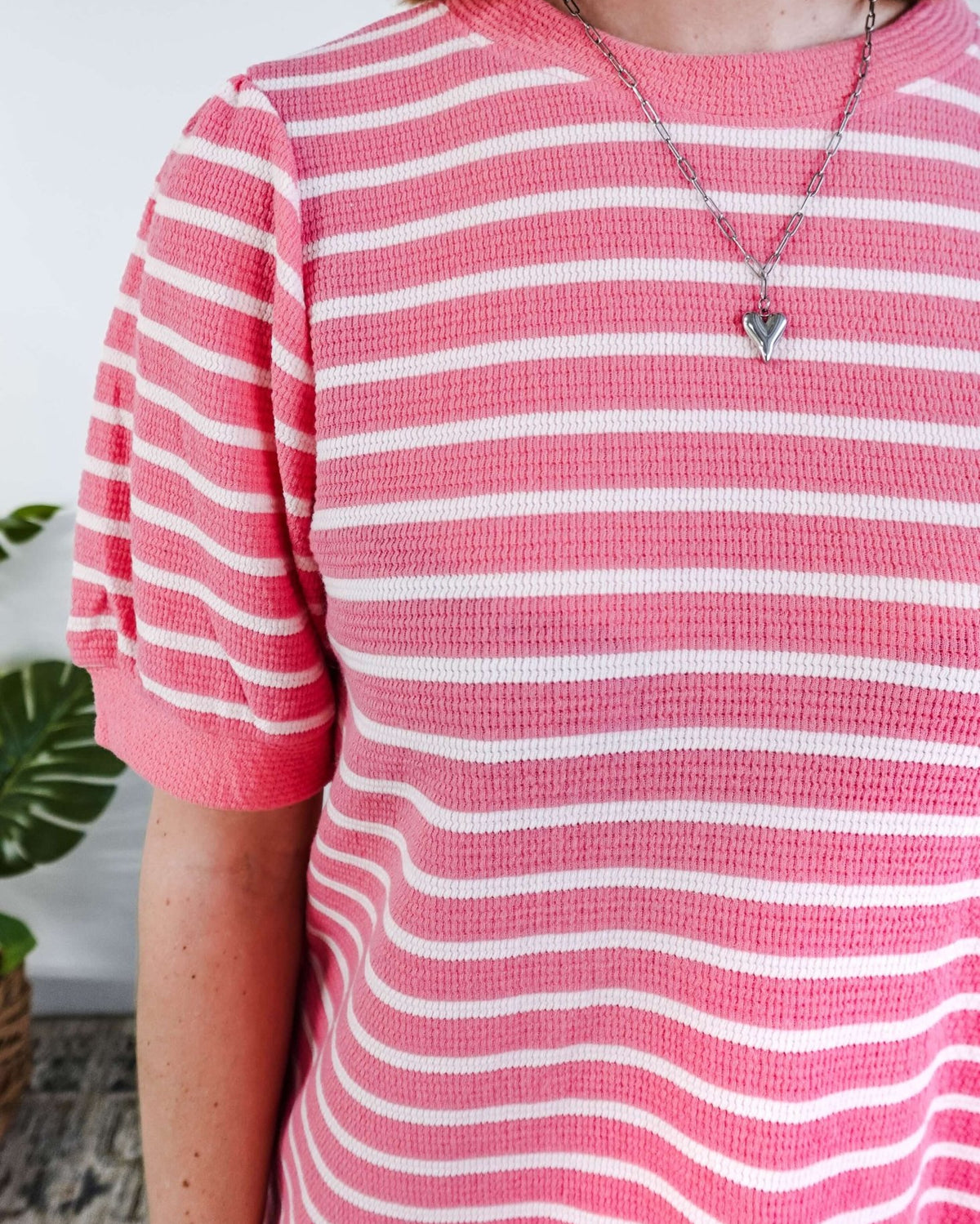 Close up of a woman wearing a pink and white striped dress with puffed sleeves in a bedroom setting.