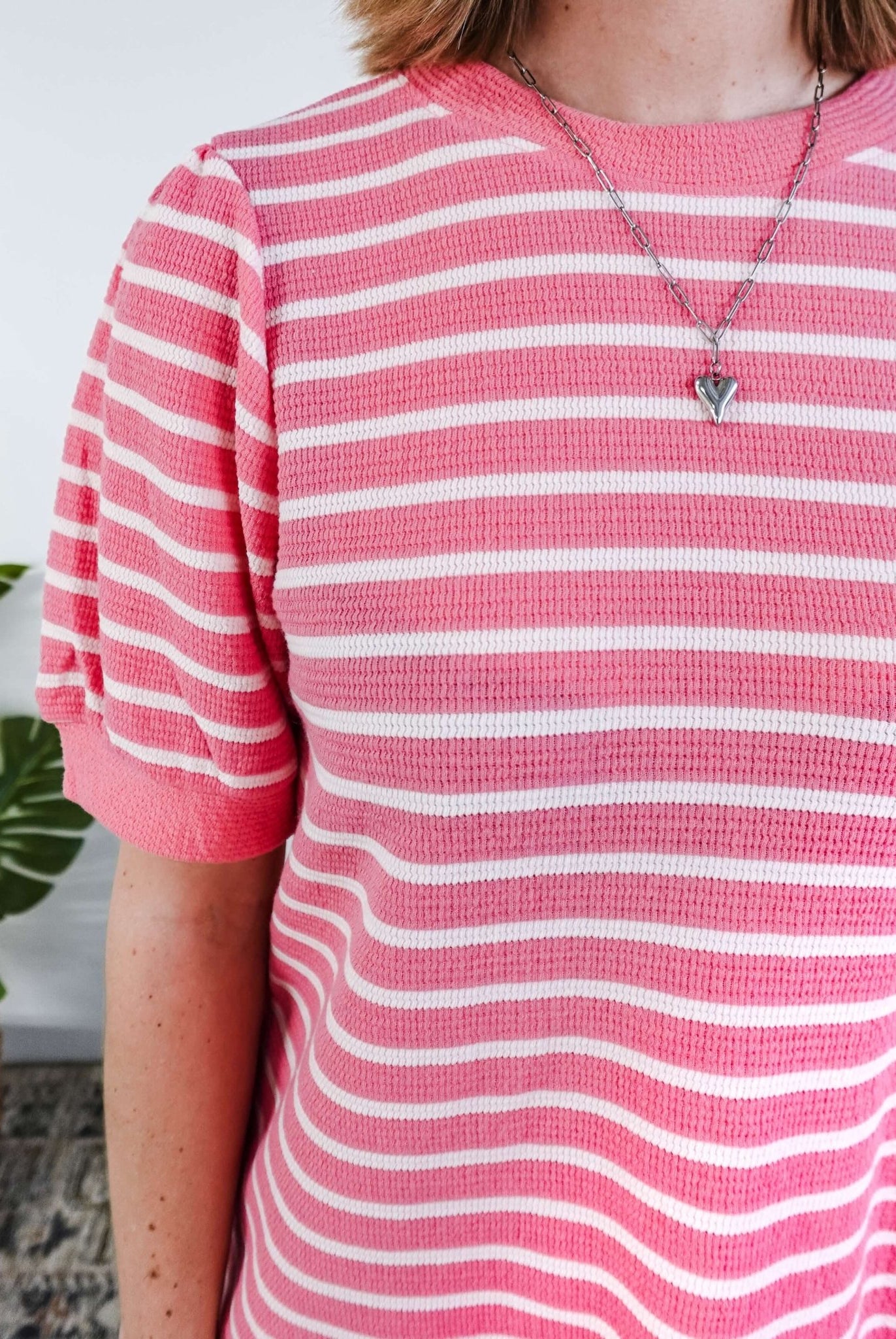 Close up of a woman wearing a pink and white striped dress with puffed sleeves in a bedroom setting.