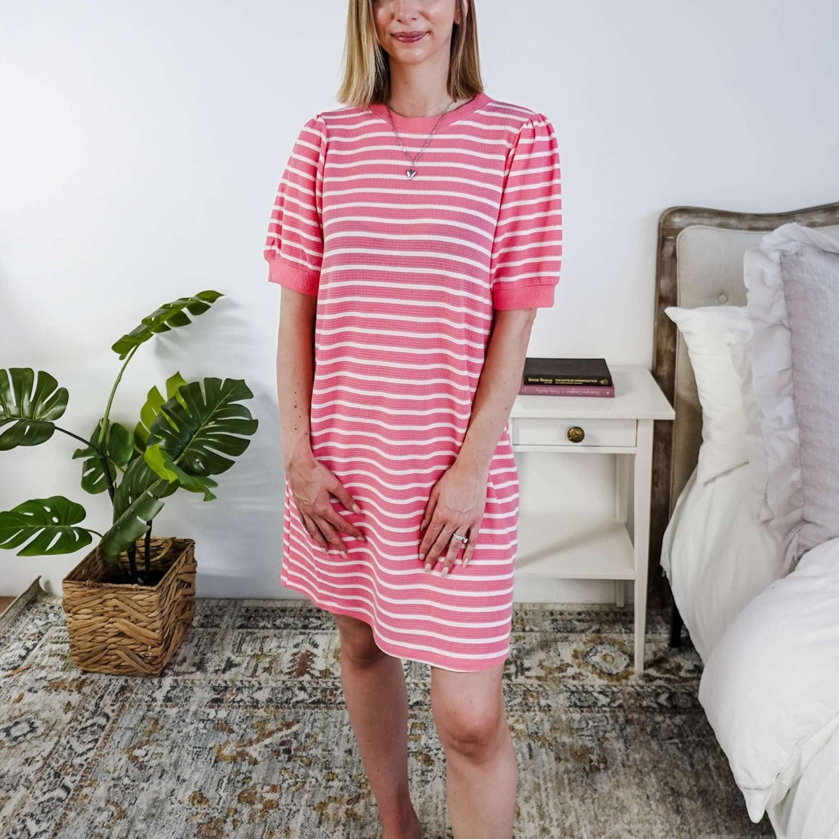 Woman wearing a pink and white striped dress with puffed sleeves in a bedroom setting.
