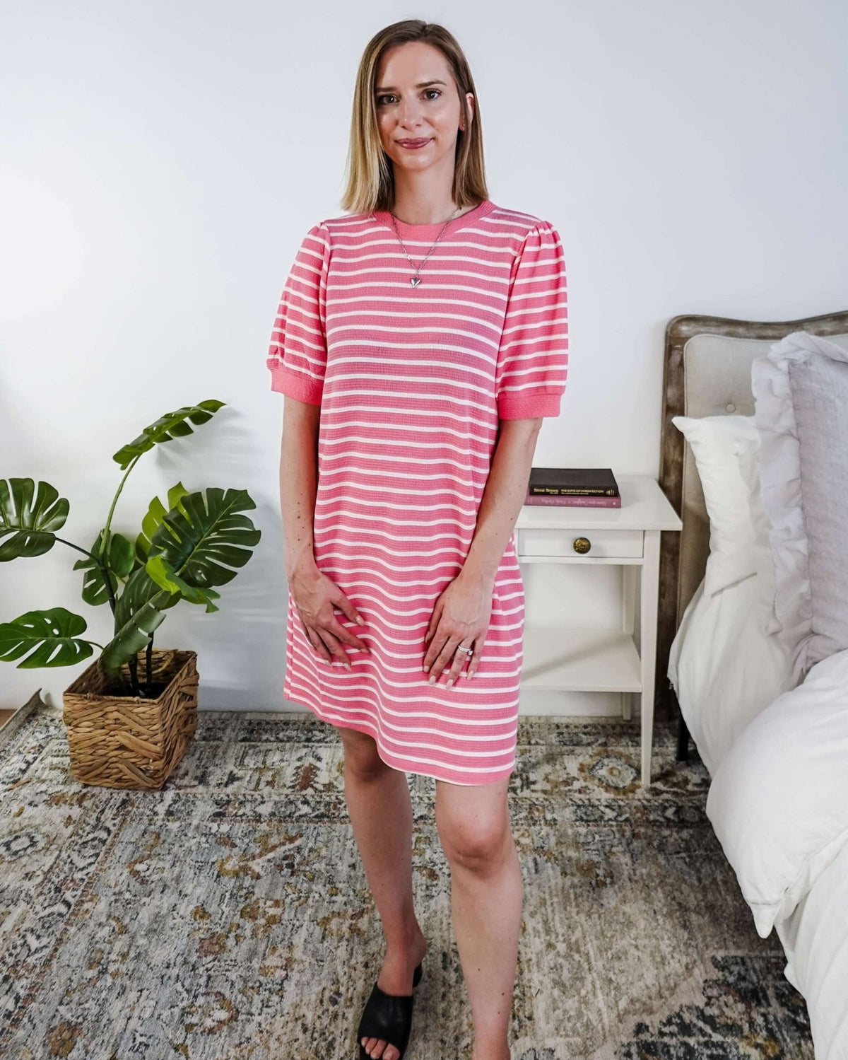 Woman wearing a pink and white striped dress with puffed sleeves in a bedroom setting.