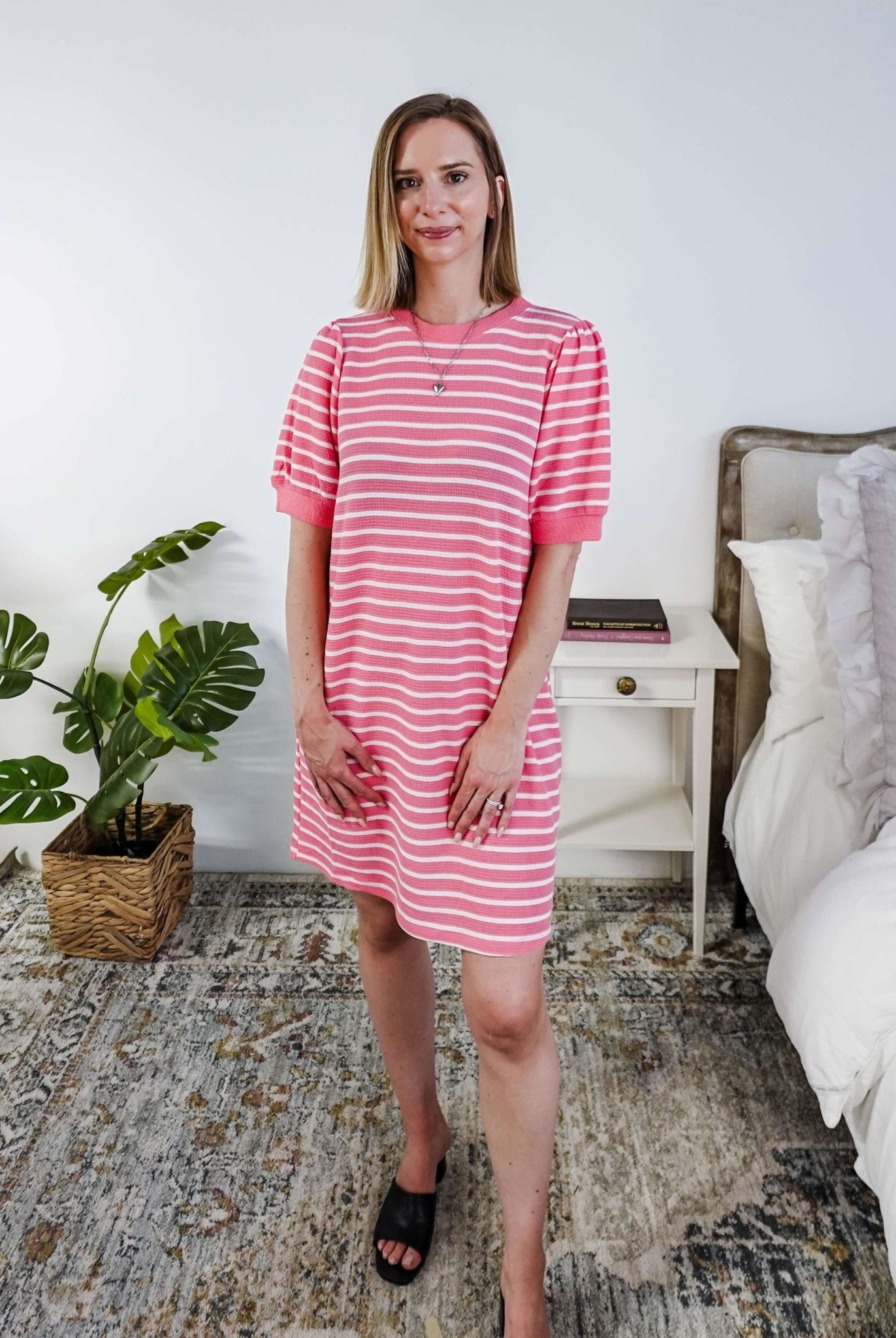Woman wearing a pink and white striped dress with puffed sleeves in a bedroom setting.