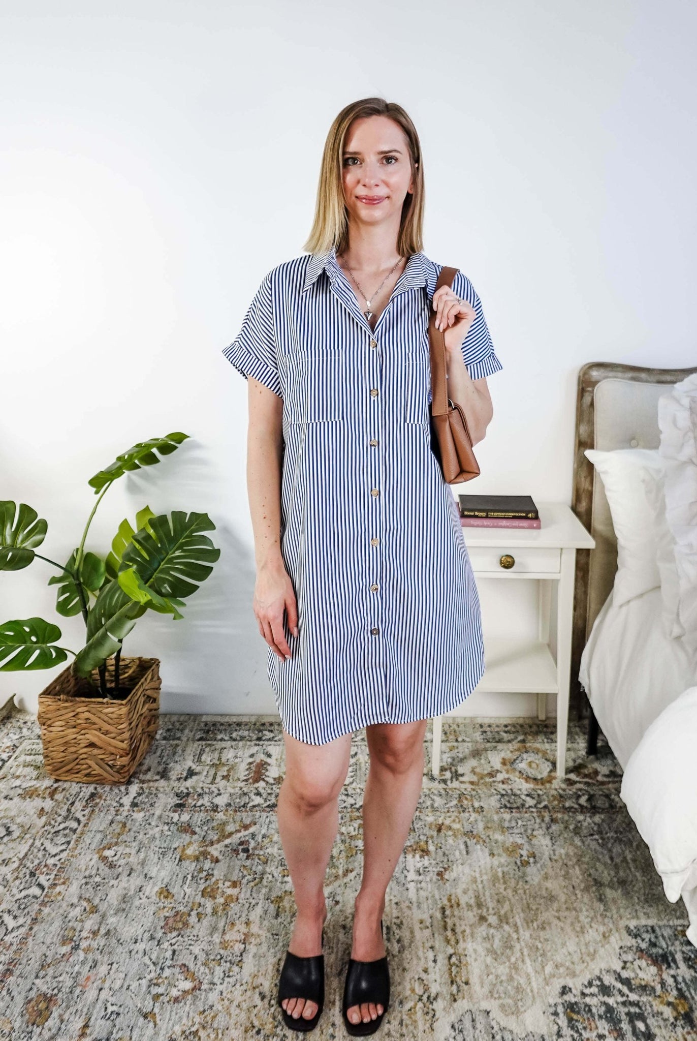 Woman in a blue and white striped dress holding a brown bag in a bedroom setting. Scarlett Ellie Collared Button-Up Short Sleeve Dress | Cloud Nine Pajamas