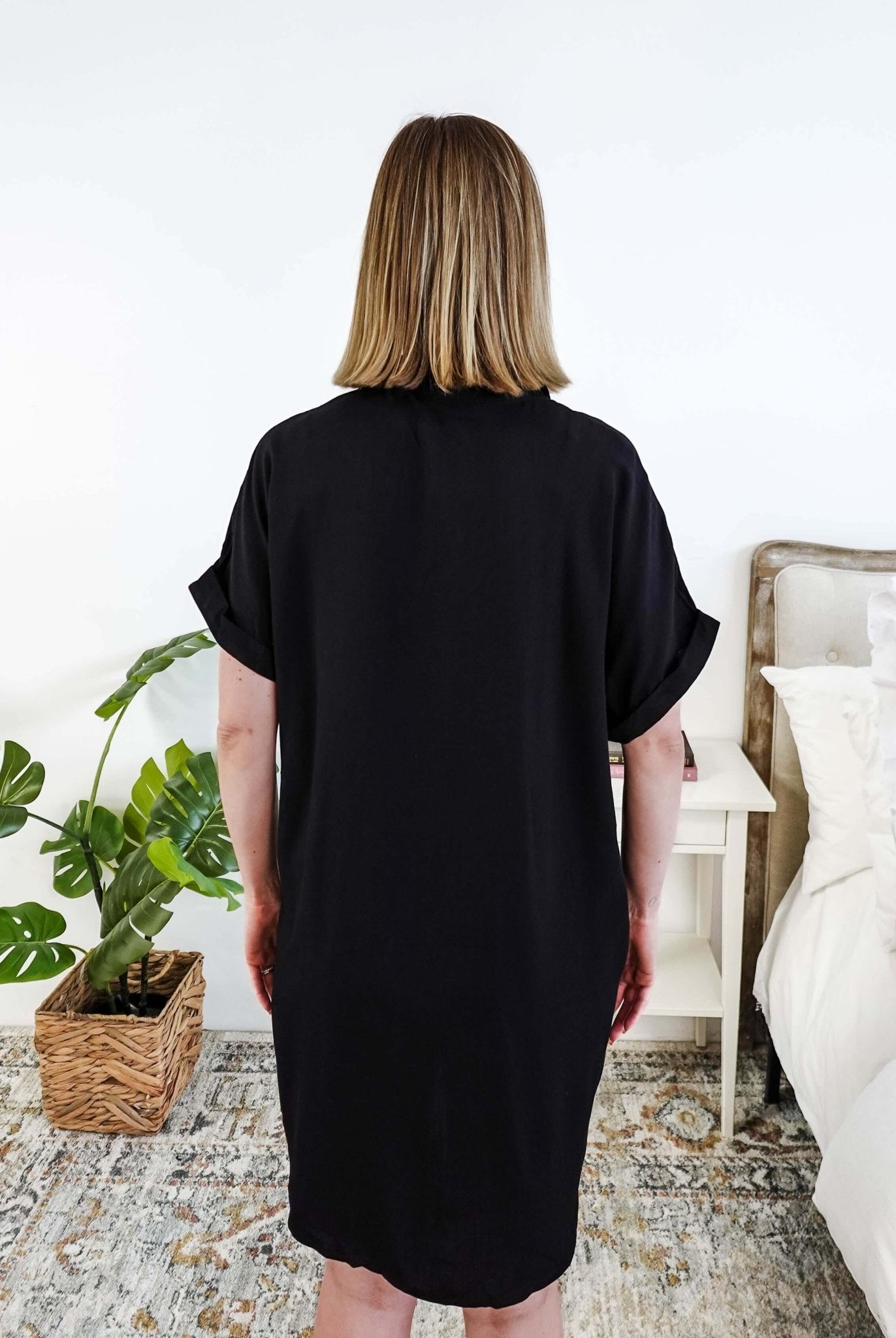 Person wearing a black dress standing in a bedroom with a plant and bed in the background Scarlett Ellie Collared Button-Up Short Sleeve Dress | Cloud Nine Pajamas showing back view