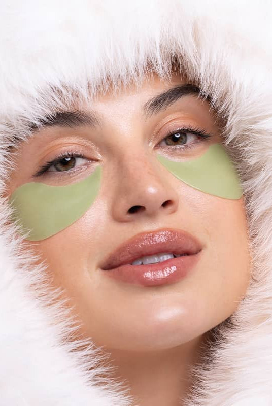 Woman wearing green eye patches with a white hood, Patchology Cool Crush Hydrogel Eye Patch single pair depuffing treatment