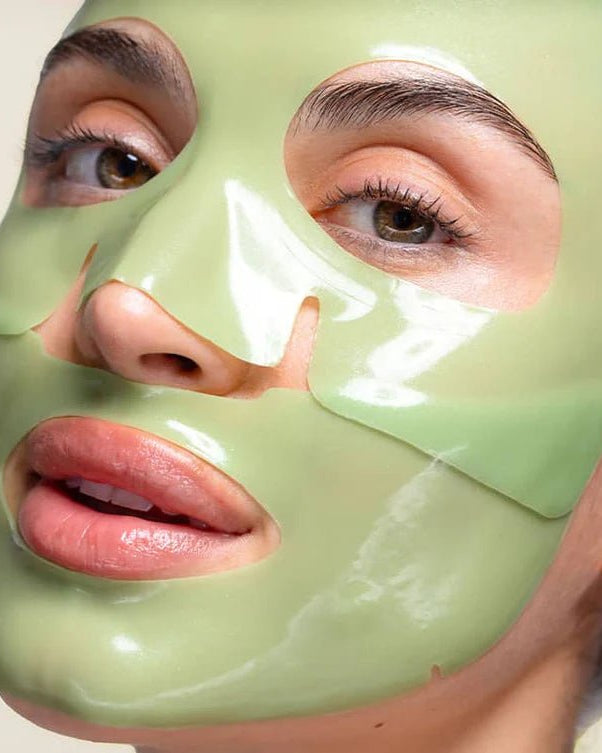 Person wearing a green face mask with a neutral background, Patchology Cool Crush cryo-inspired hydrogel face mask depuffing