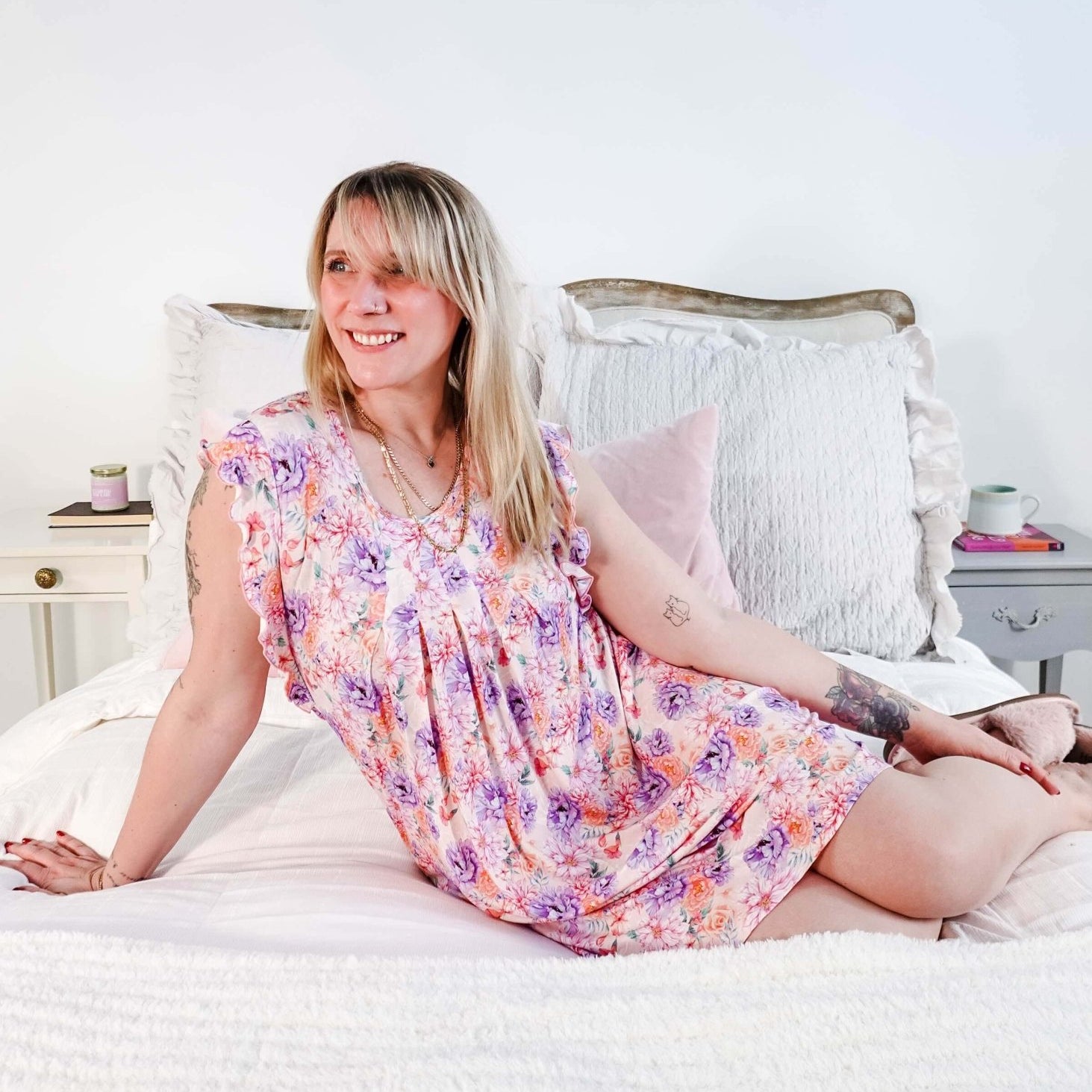 Dream In Blooms Flutter Bamboo Nightgown displayed on a smiling woman sitting on a bed, showcasing romantic sleepwear.