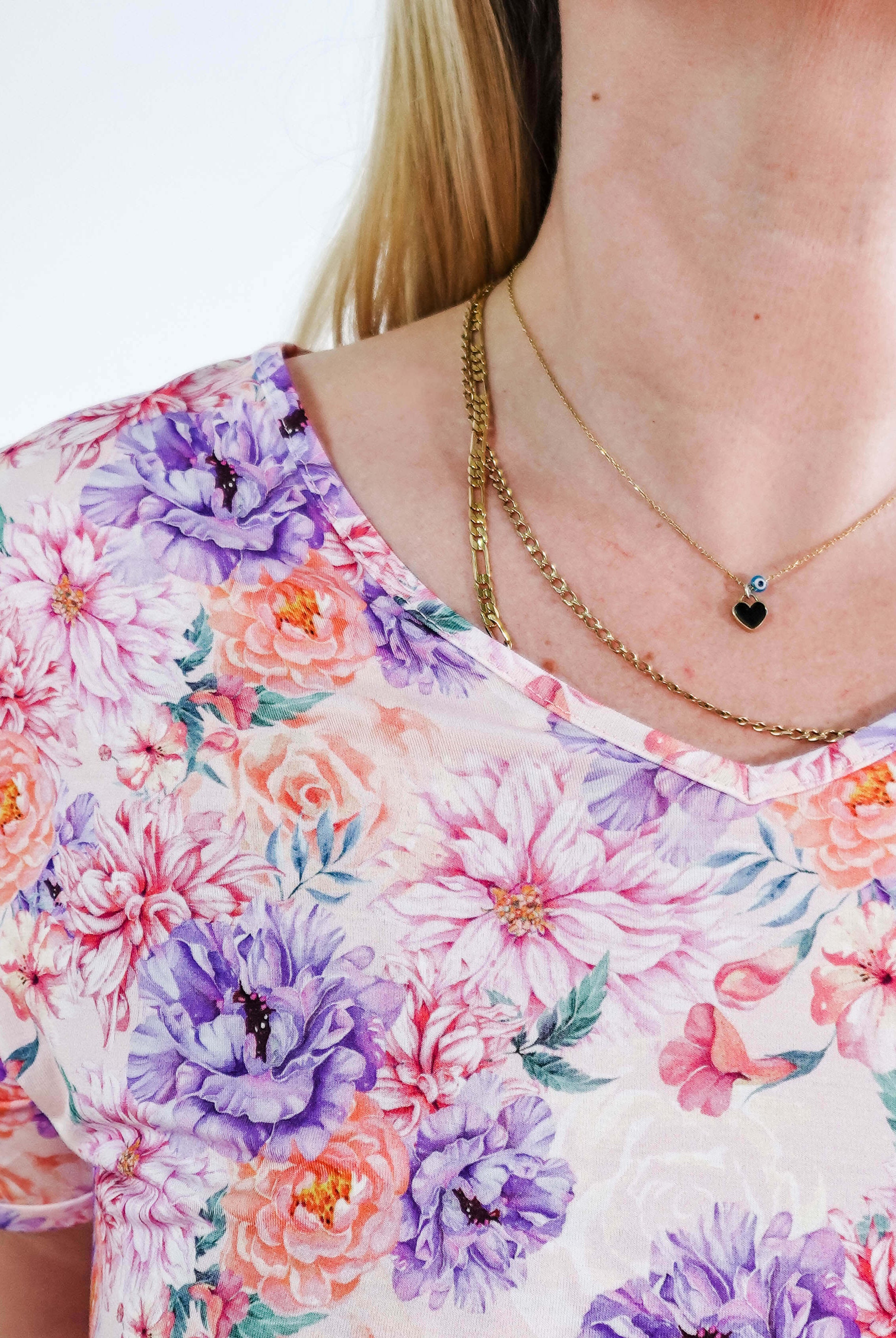 Close-up of a woman wearing the Dream in Blooms V Neck Nightshirt With Pockets featuring vibrant floral patterns and layered necklaces.