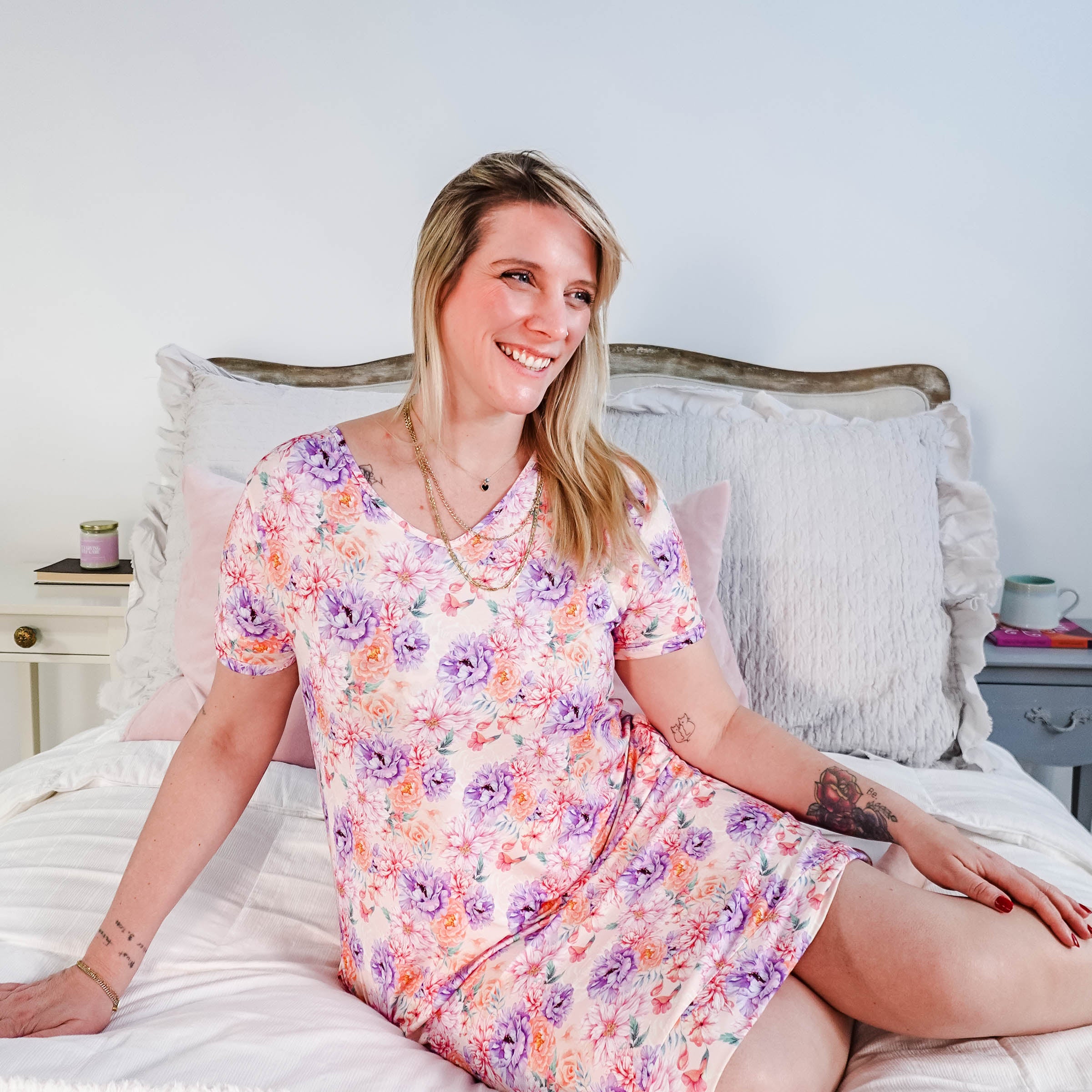 Dream in Blooms V Neck Nightshirt With Pockets worn by a woman sitting on a bed, featuring a floral design.