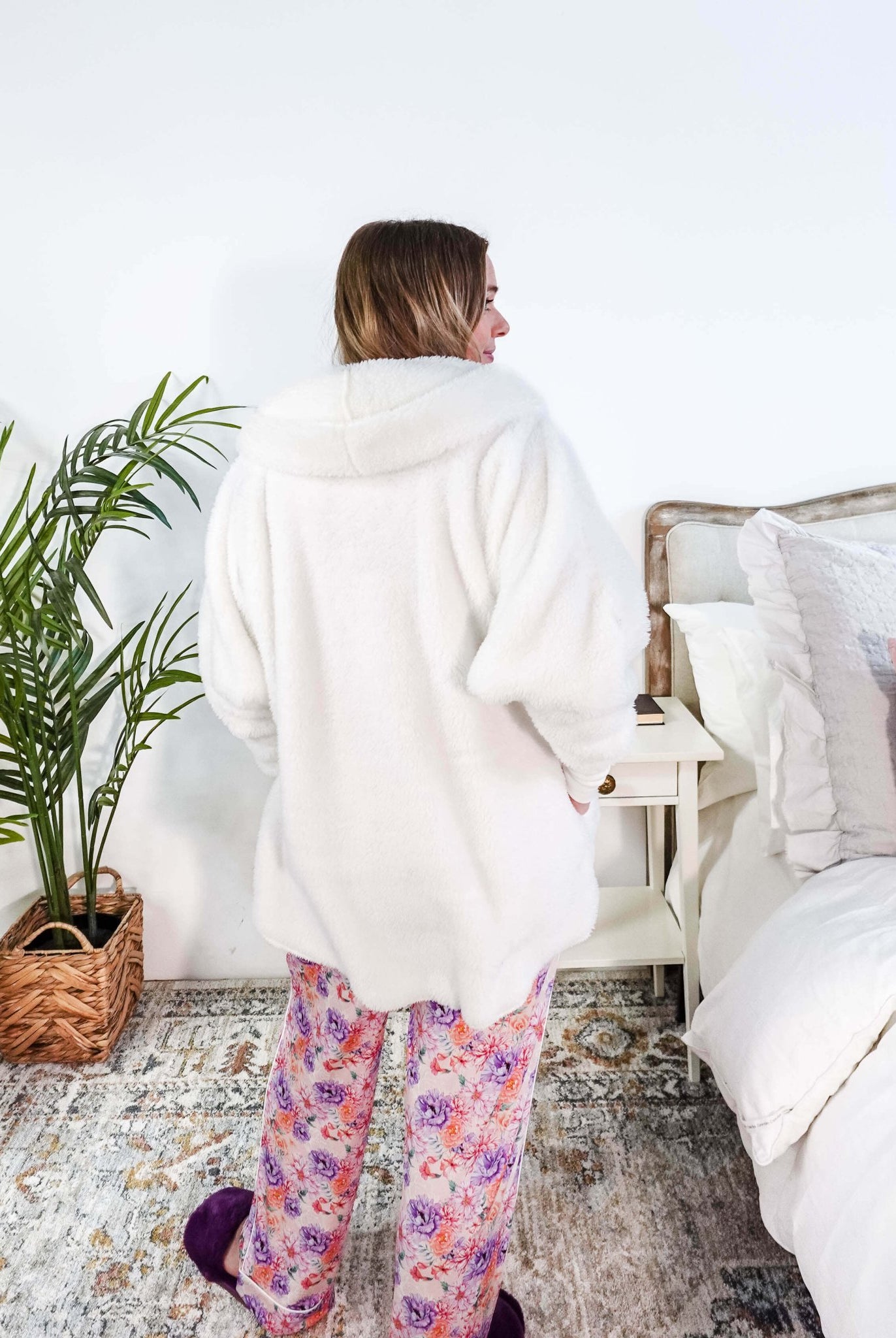 Essential Hooded Fluffy Cozy Cardigan with Pockets worn by a woman with floral pajamas in a cozy bedroom setting showing back of cardigan