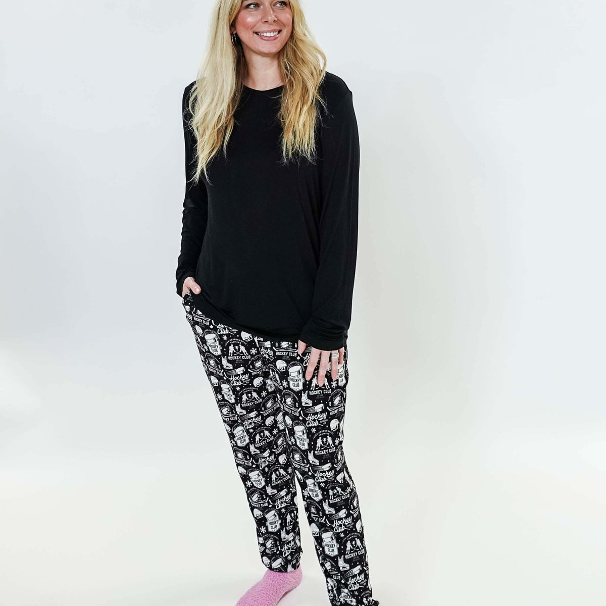 Woman wearing He Scores Hockey Print Unisex Bamboo Jogger with a black long sleeve top and pink slippers.