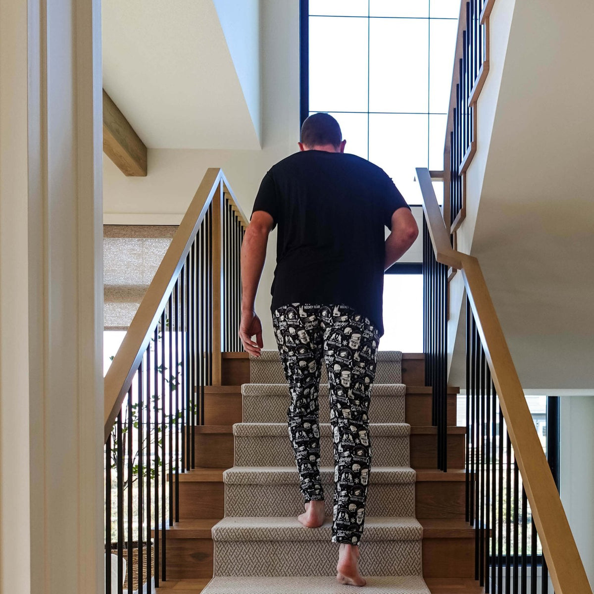 Man wearing He Scores Hockey Print Unisex Bamboo Jogger walking up stairs in a modern home.