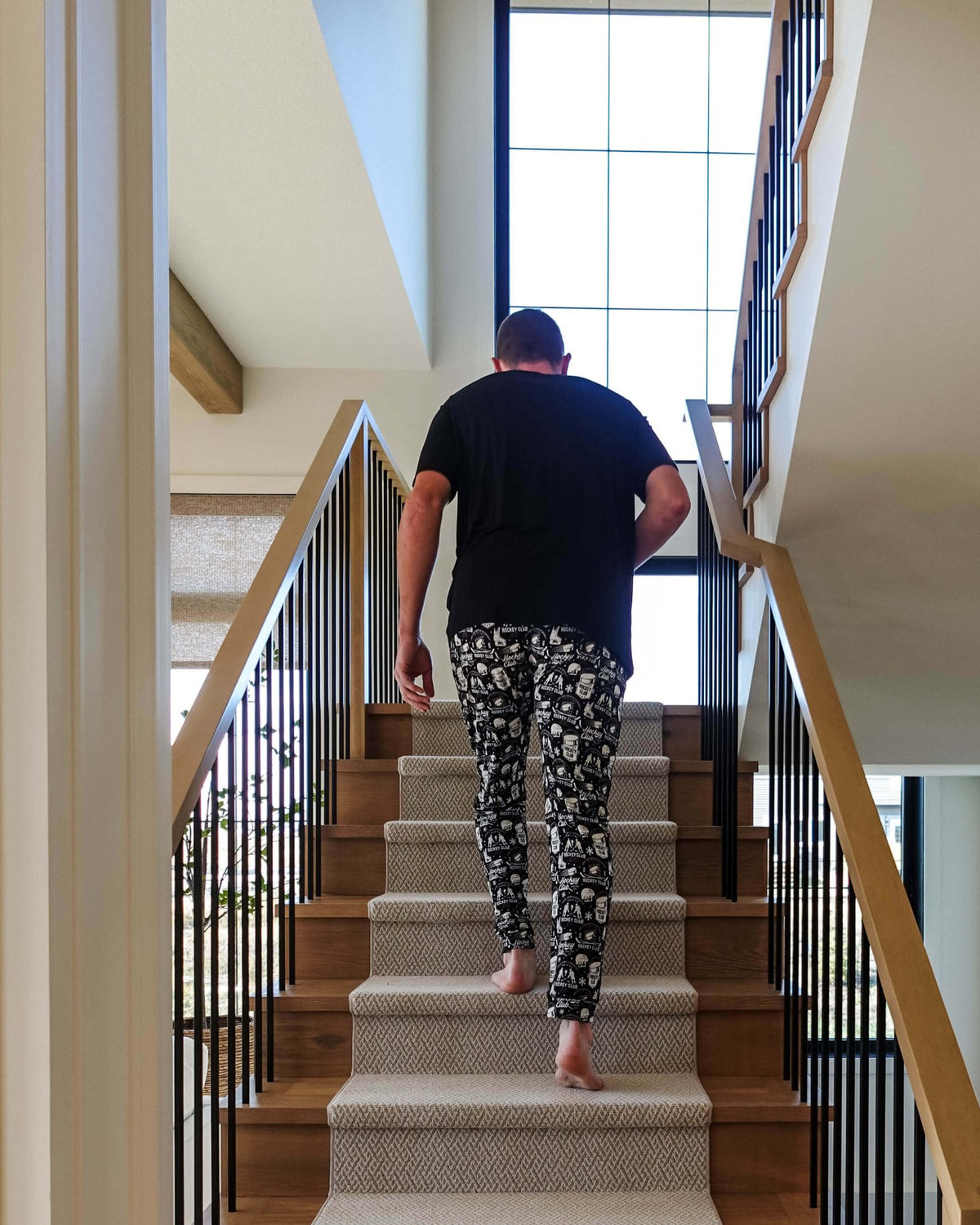 Man wearing He Scores Hockey Print Unisex Bamboo Jogger walking up stairs in a modern home.