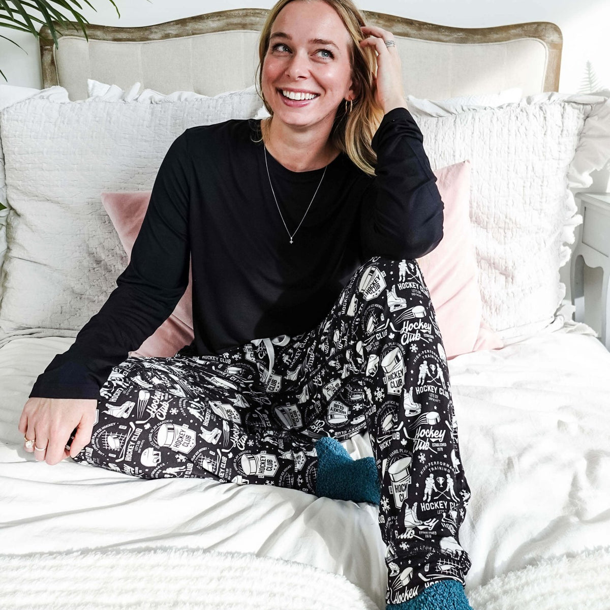 He Scores Hockey Print Unisex Bamboo Jogger worn by a smiling woman sitting on a bed with cozy decor.