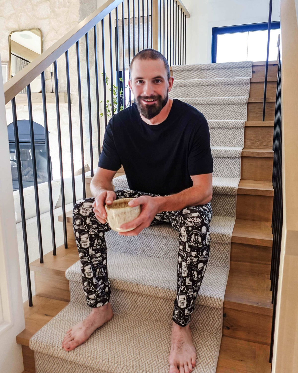 Man sitting on stairs wearing He Scores Hockey Print Unisex Bamboo Jogger and holding a bowl.