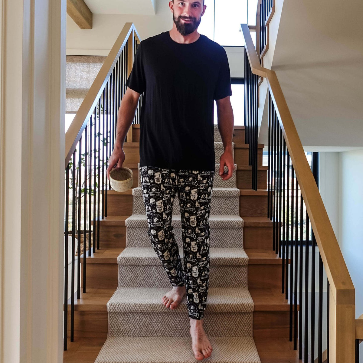 Man in He Scores Hockey Print Unisex Bamboo Jogger descending stairs with a drink in hand.