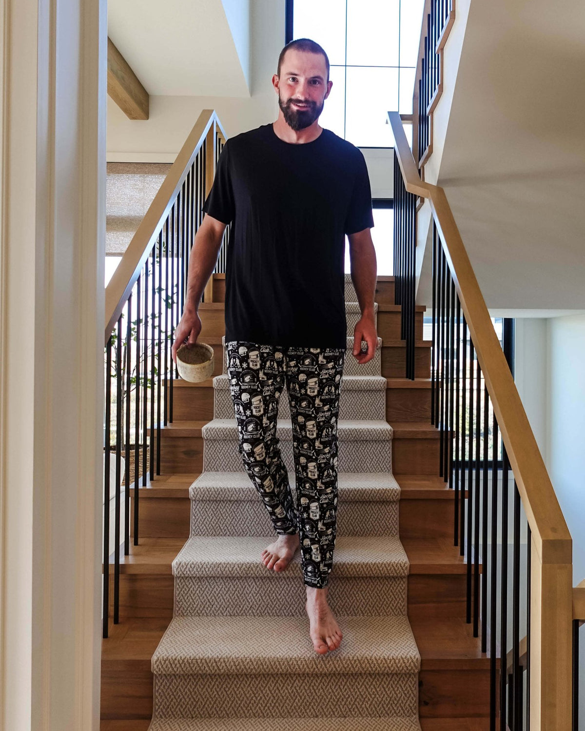 Man in He Scores Hockey Print Unisex Bamboo Jogger descending stairs with a drink in hand.