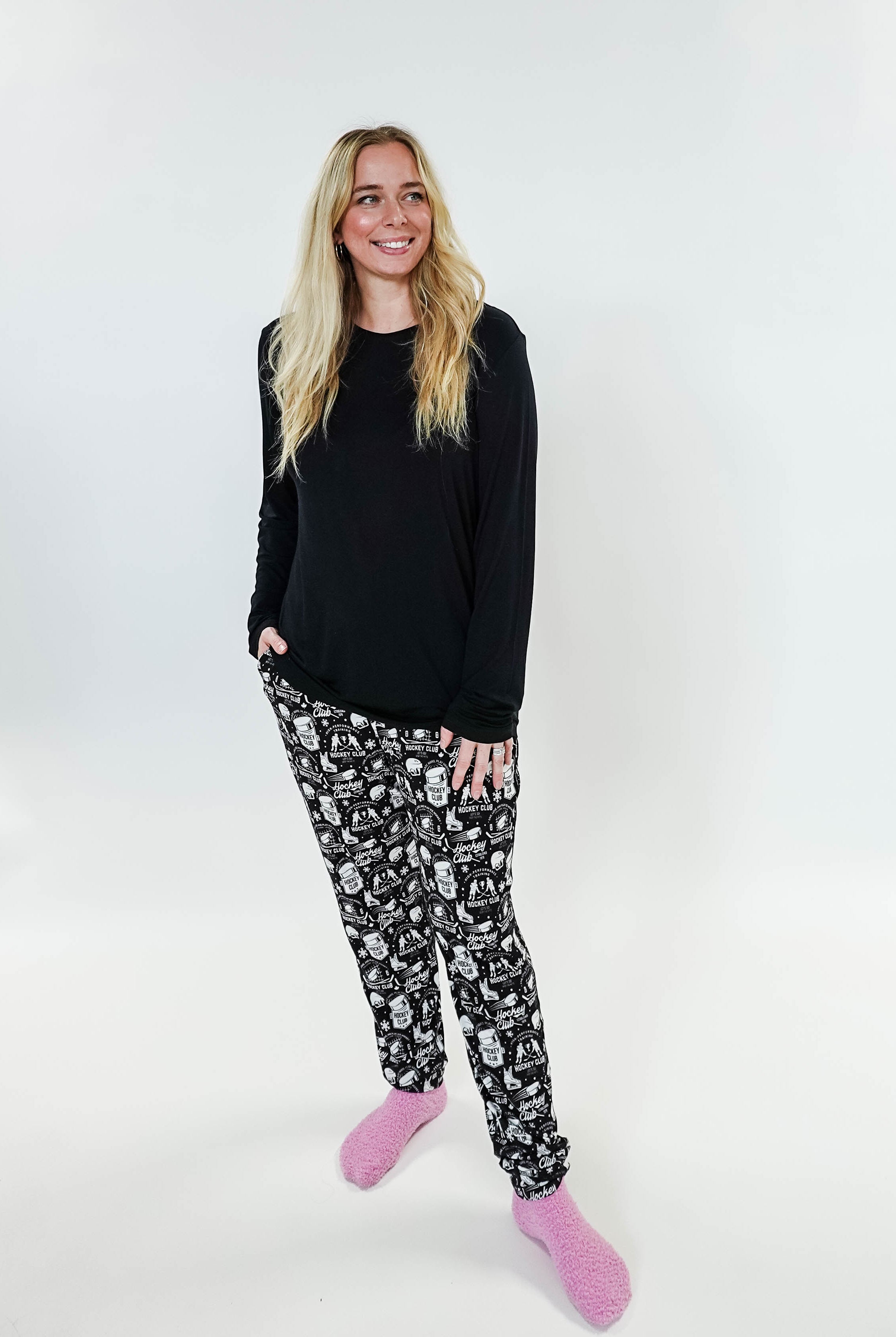 Woman wearing He Scores Hockey Print Unisex Bamboo Jogger with a black long sleeve top and pink slippers.