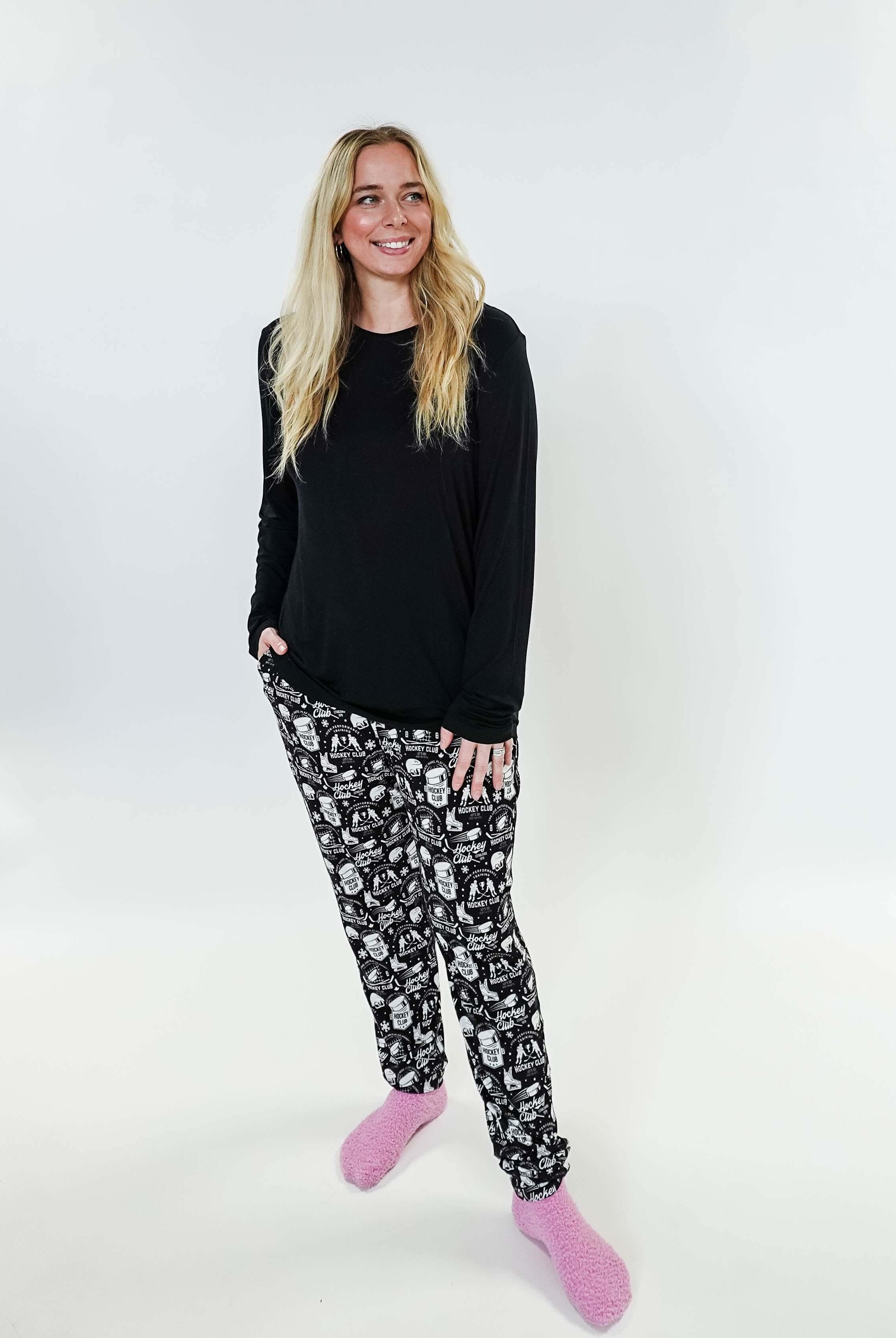 Woman wearing He Scores Hockey Print Unisex Bamboo Jogger with a black long sleeve top and pink slippers.