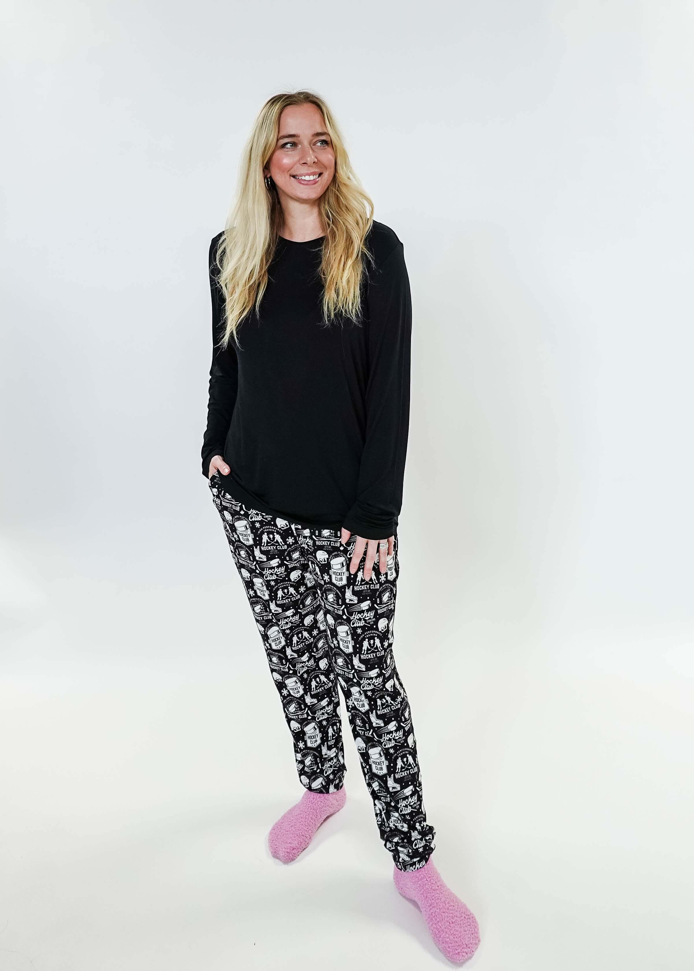 Woman wearing He Scores Hockey Print Unisex Bamboo Jogger with a black long sleeve top and pink slippers.