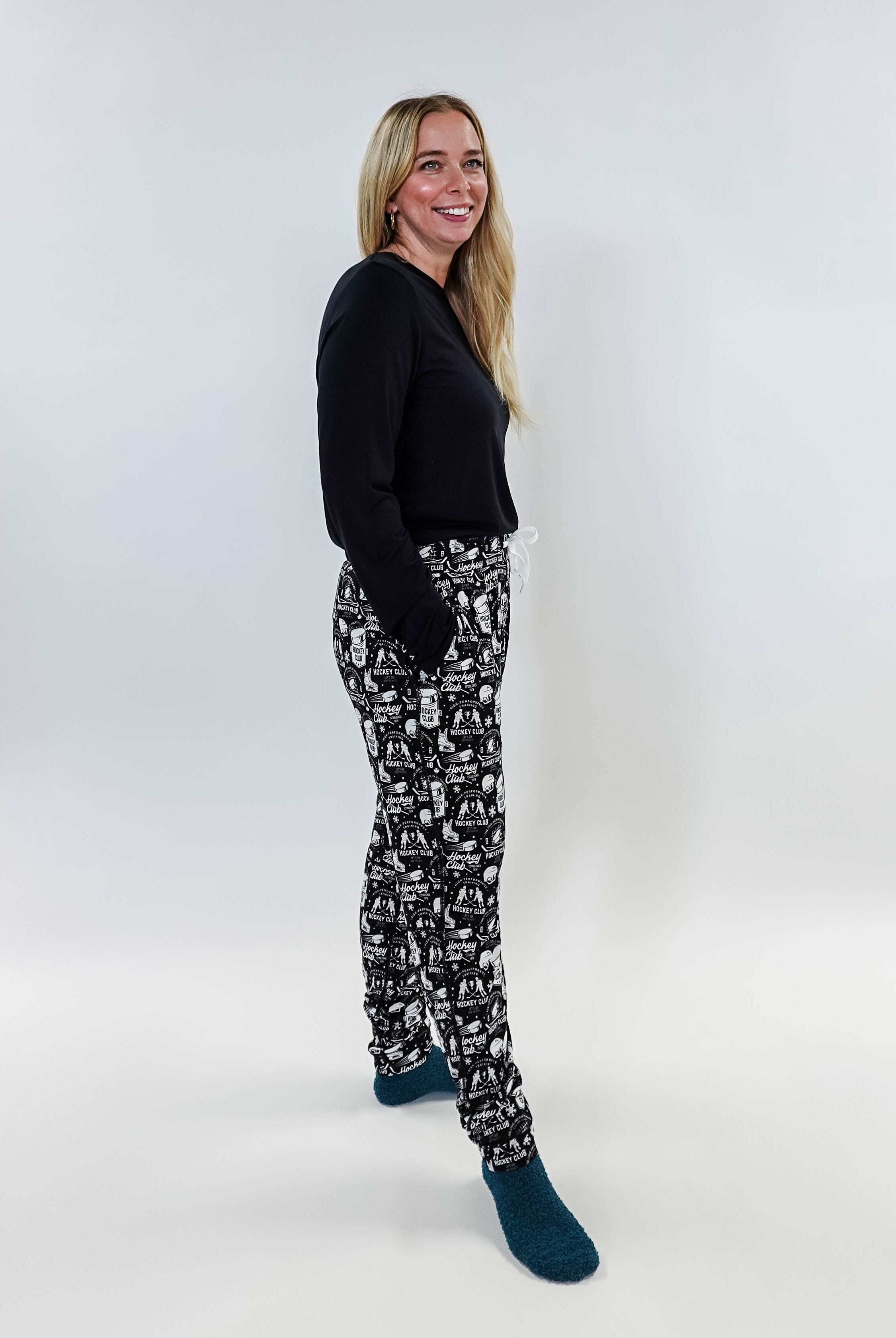 Female model wearing He Scores Hockey Print Unisex Bamboo Jogger with a black long-sleeve top and blue socks.