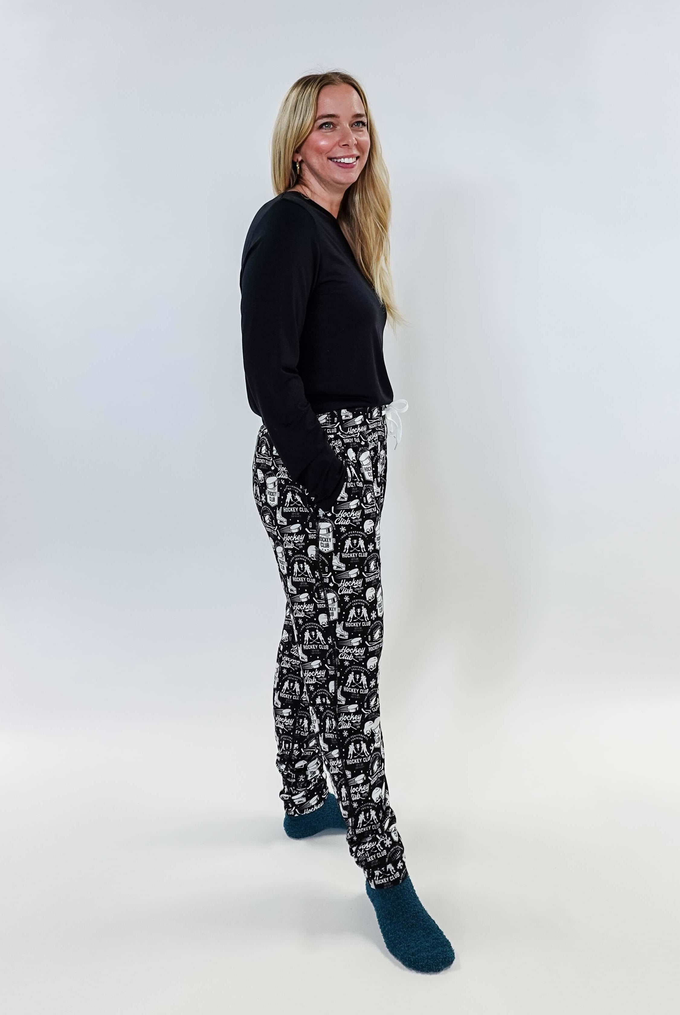 Female model wearing He Scores Hockey Print Unisex Bamboo Jogger with a black long-sleeve top and blue socks.