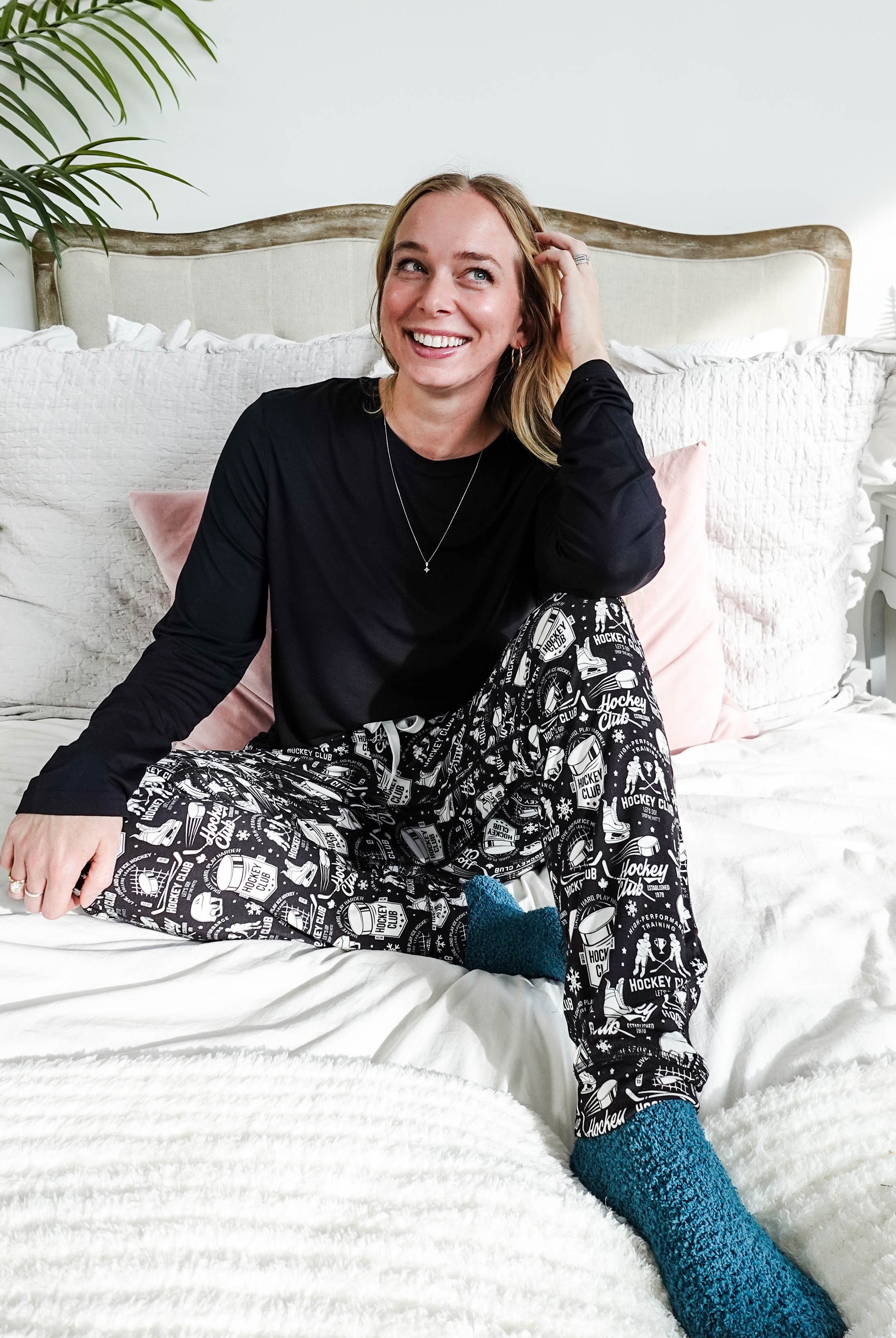 He Scores Hockey Print Unisex Bamboo Jogger worn by a smiling woman sitting on a bed with cozy decor.