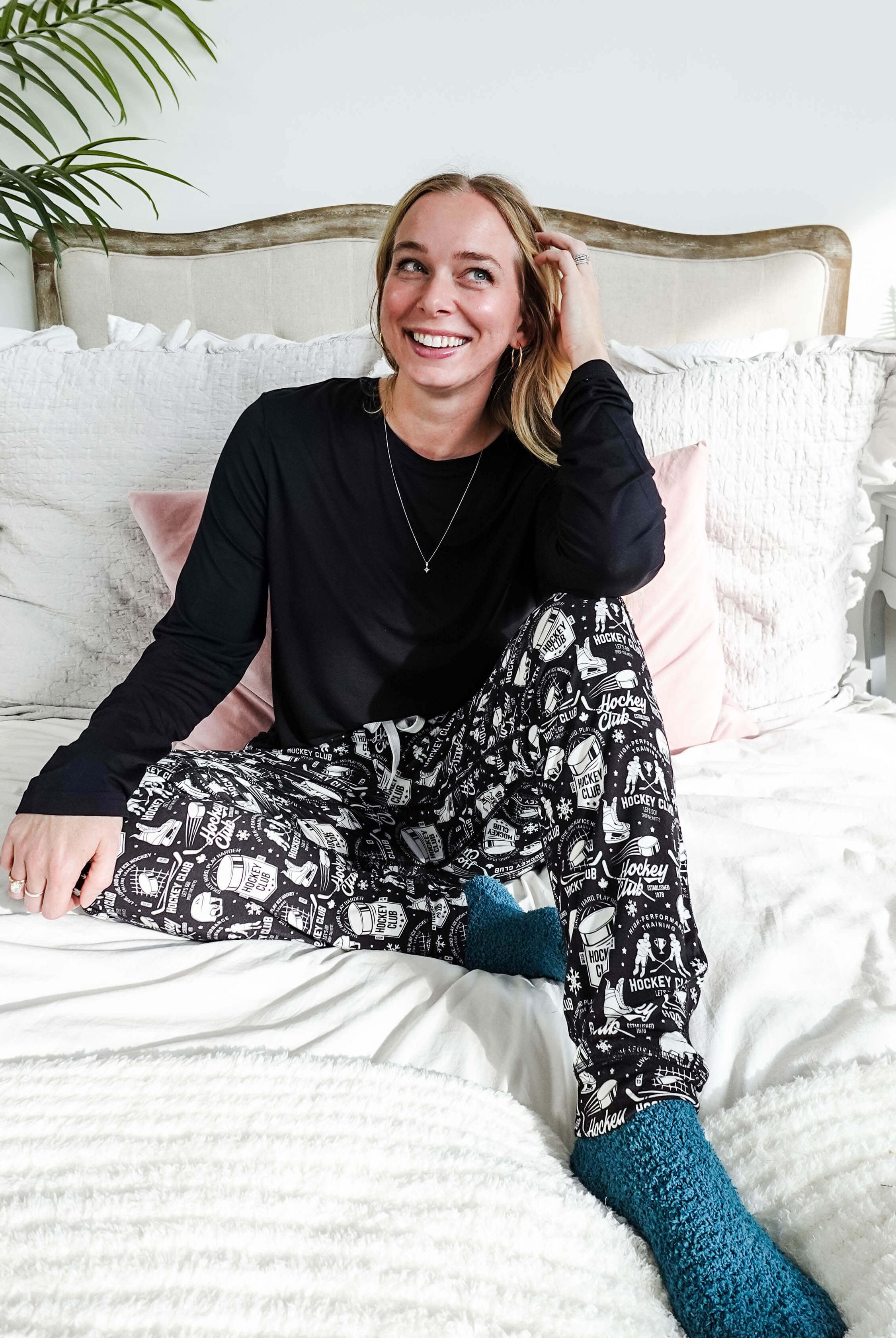 He Scores Hockey Print Unisex Bamboo Jogger worn by a smiling woman sitting on a bed with cozy decor.