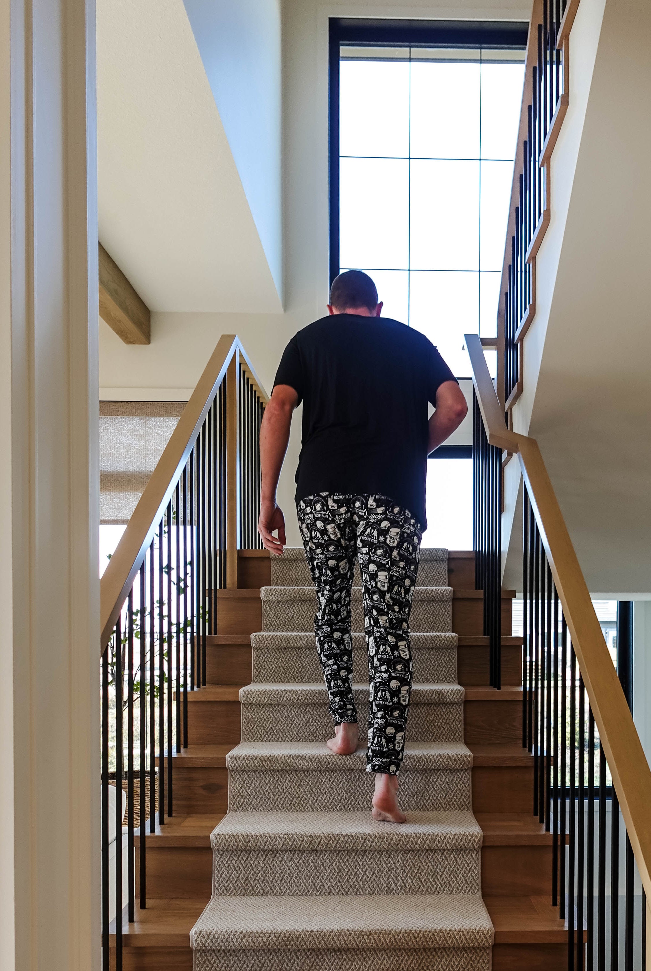 Man wearing He Scores Hockey Print Unisex Bamboo Jogger walking up stairs in a modern home.