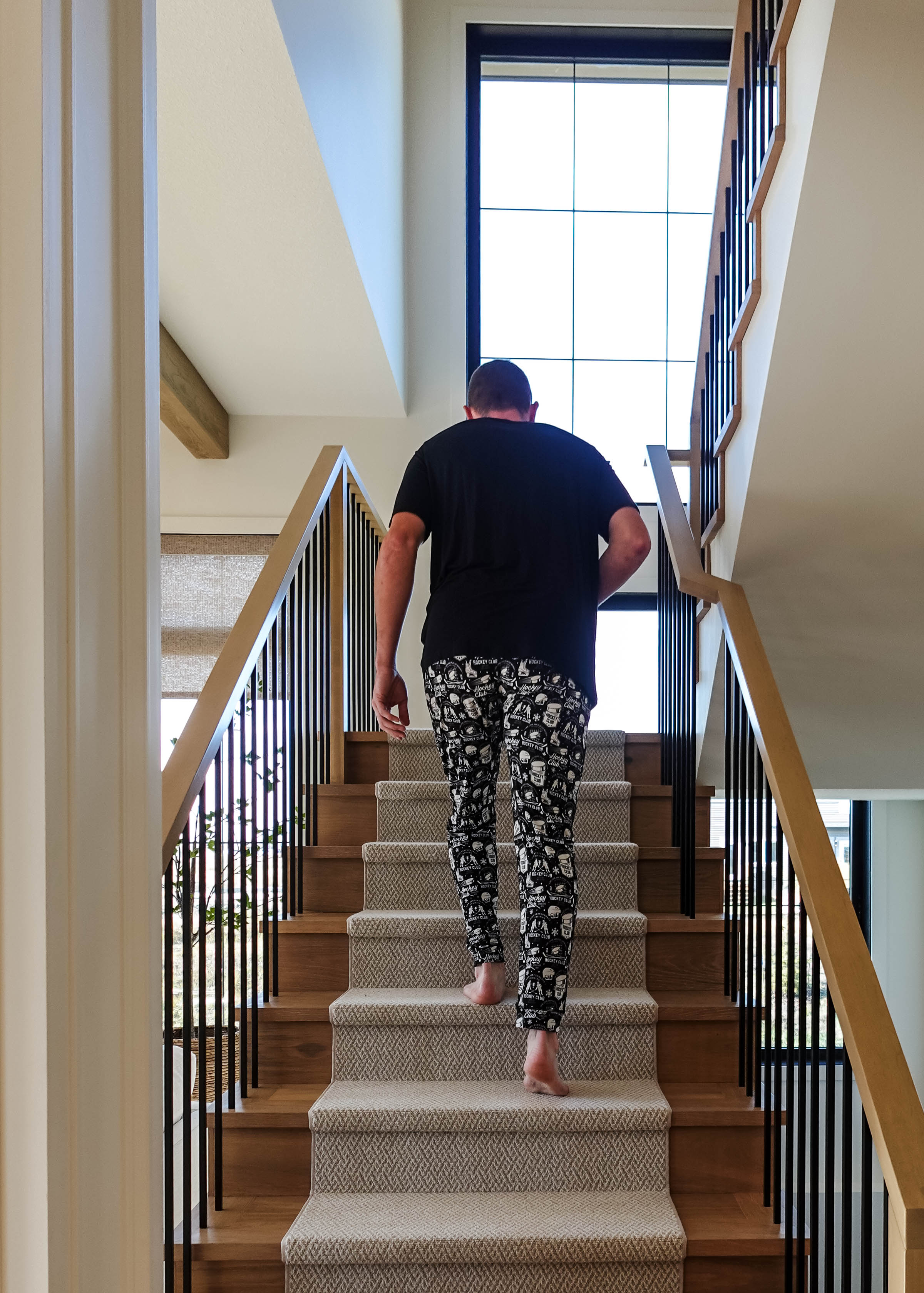 Man wearing He Scores Hockey Print Unisex Bamboo Jogger walking up stairs in a modern home.