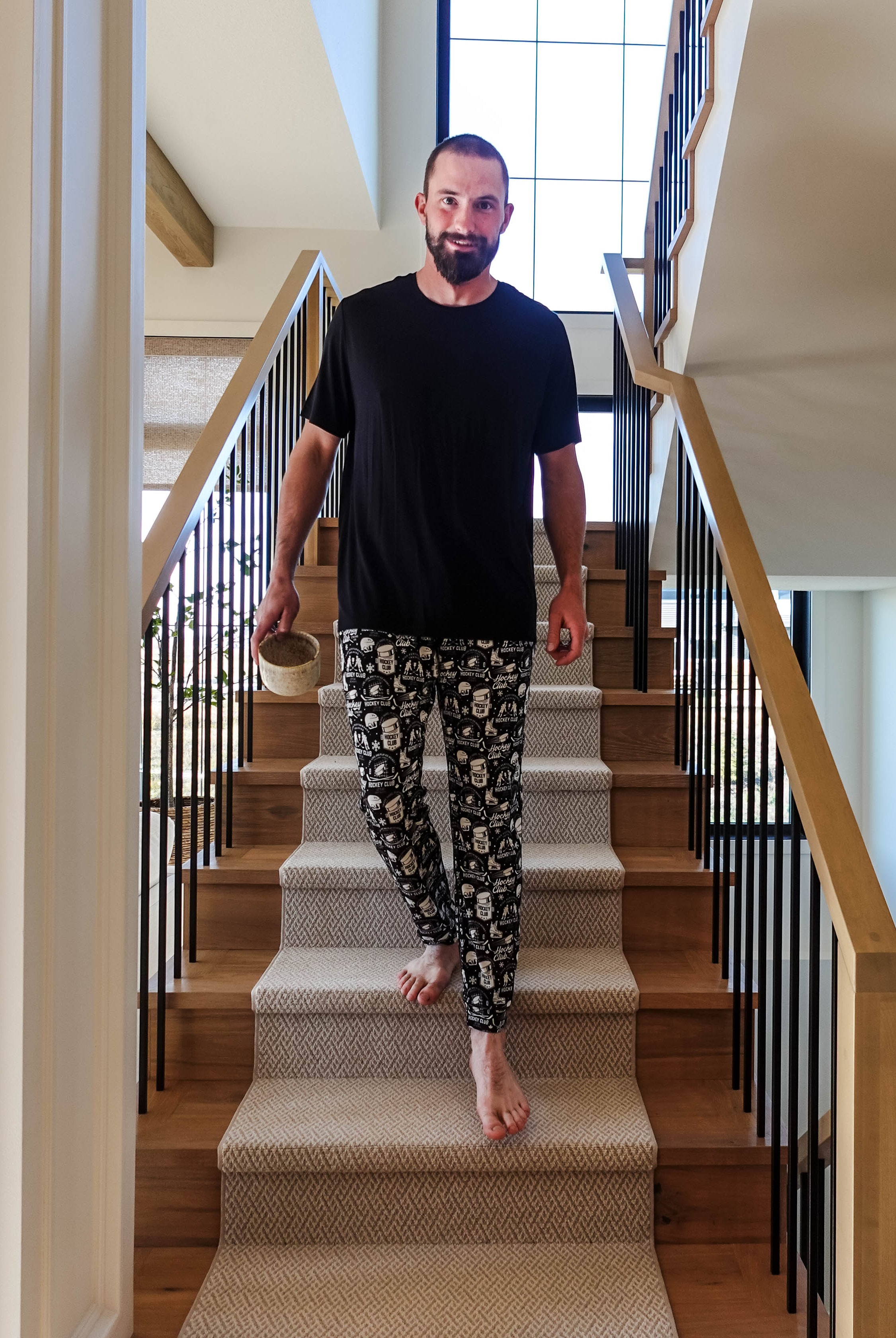 Man in He Scores Hockey Print Unisex Bamboo Jogger descending stairs with a drink in hand.