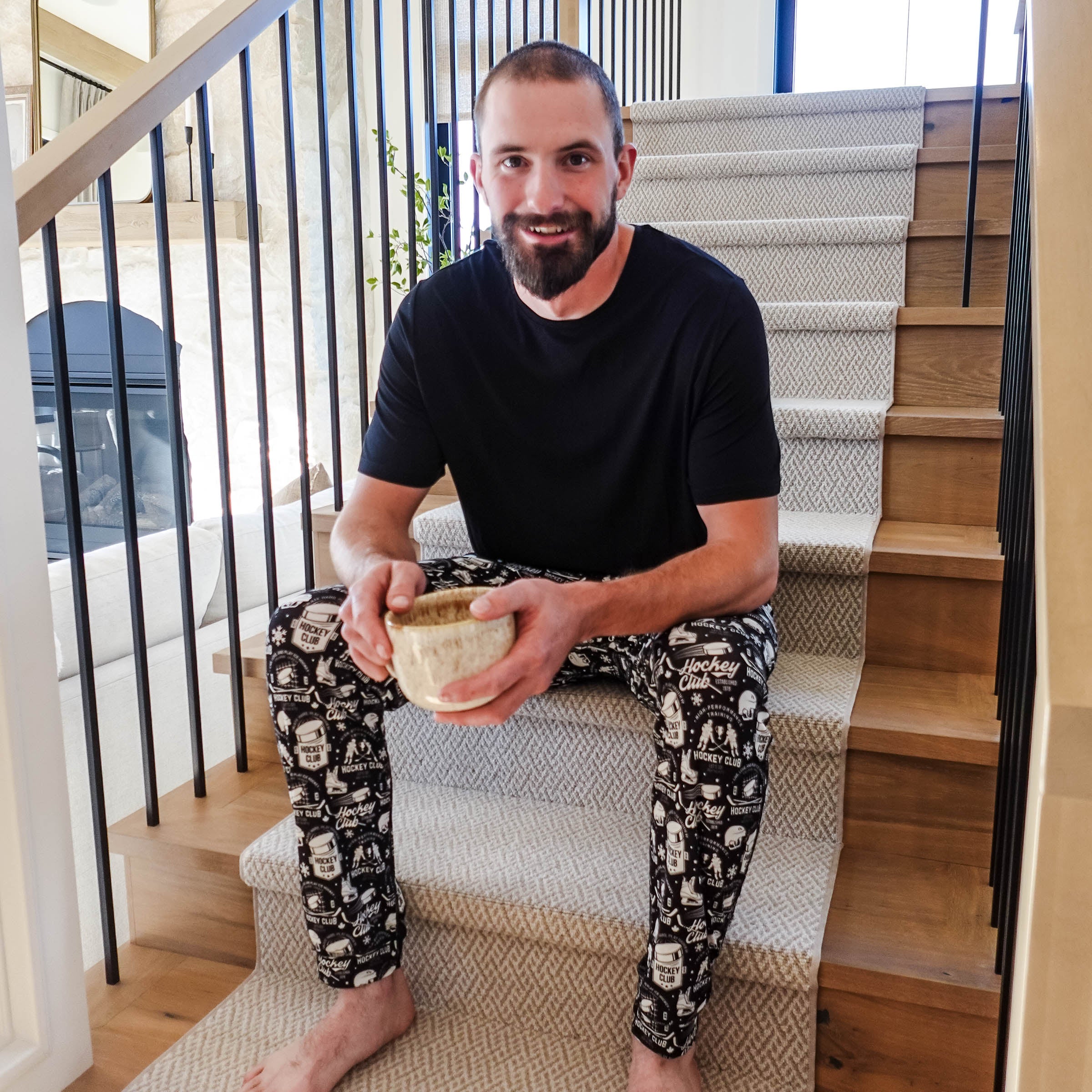 Man sitting on stairs wearing He Scores Hockey Print Unisex Bamboo Jogger and holding a bowl.