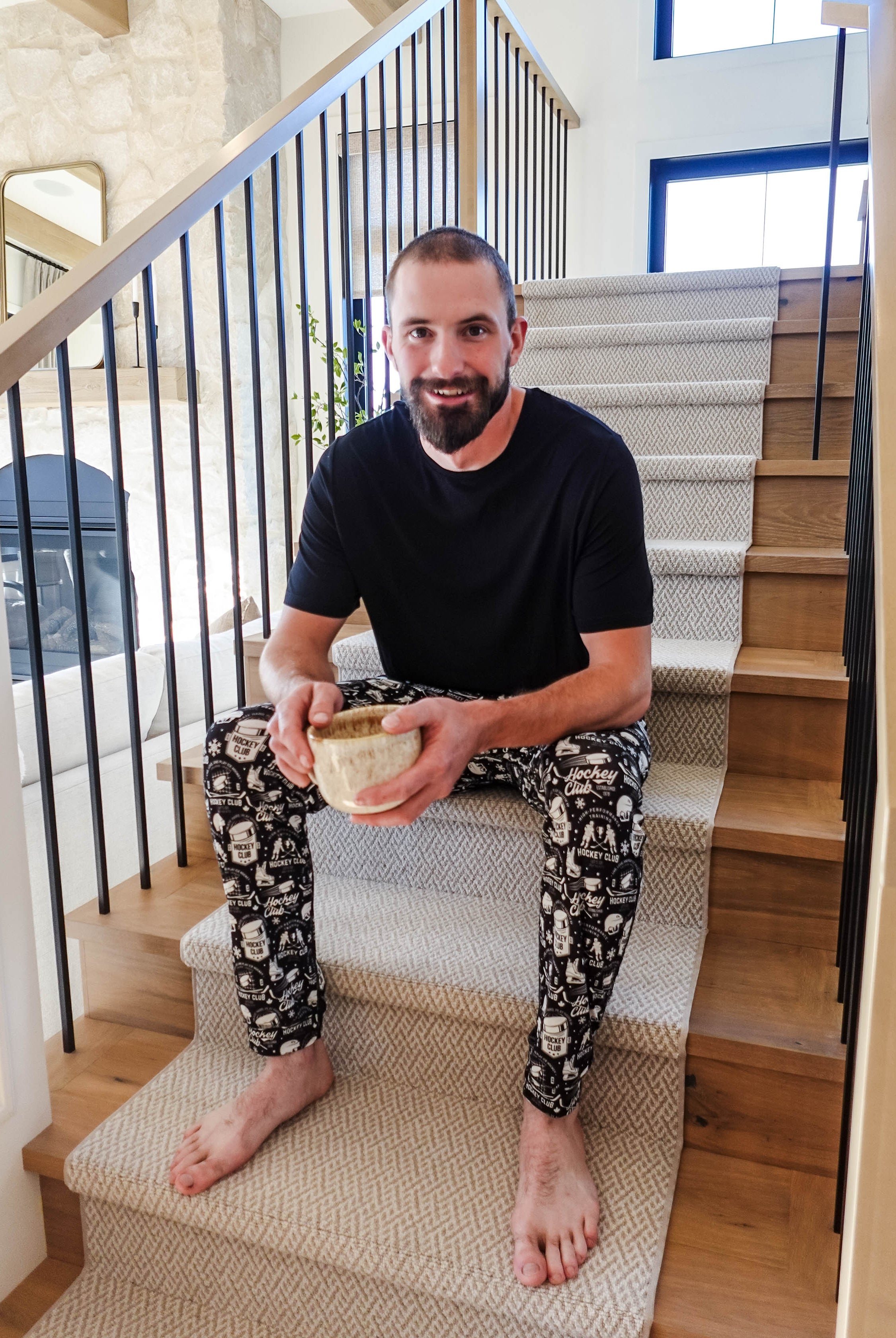 Man sitting on stairs wearing He Scores Hockey Print Unisex Bamboo Jogger and holding a bowl.