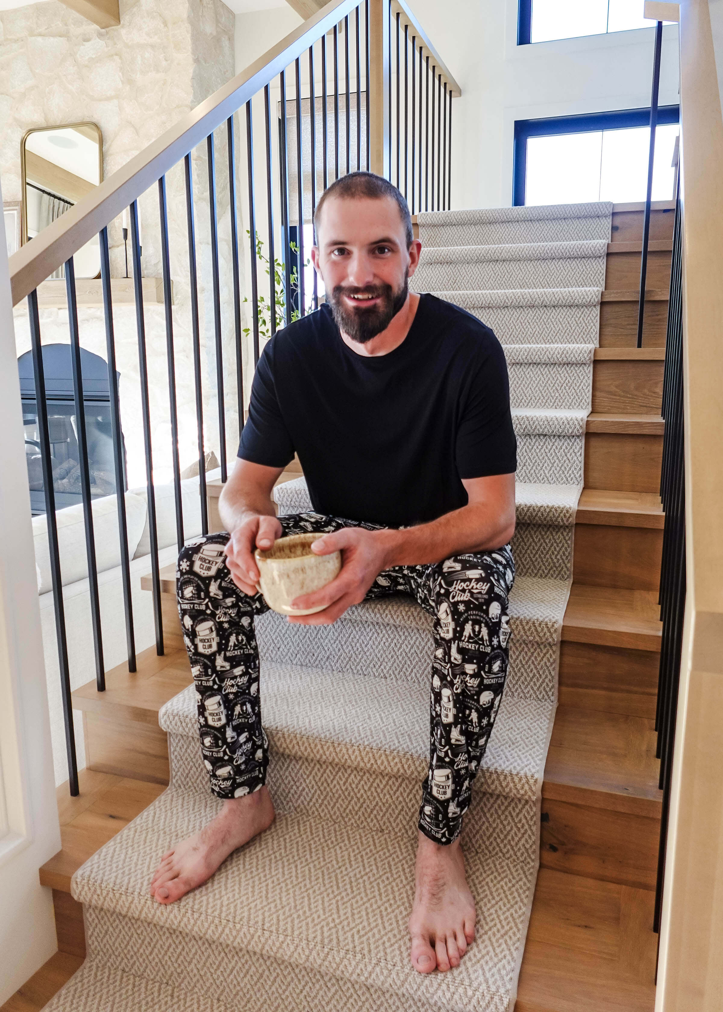 Man sitting on stairs wearing He Scores Hockey Print Unisex Bamboo Jogger and holding a bowl.