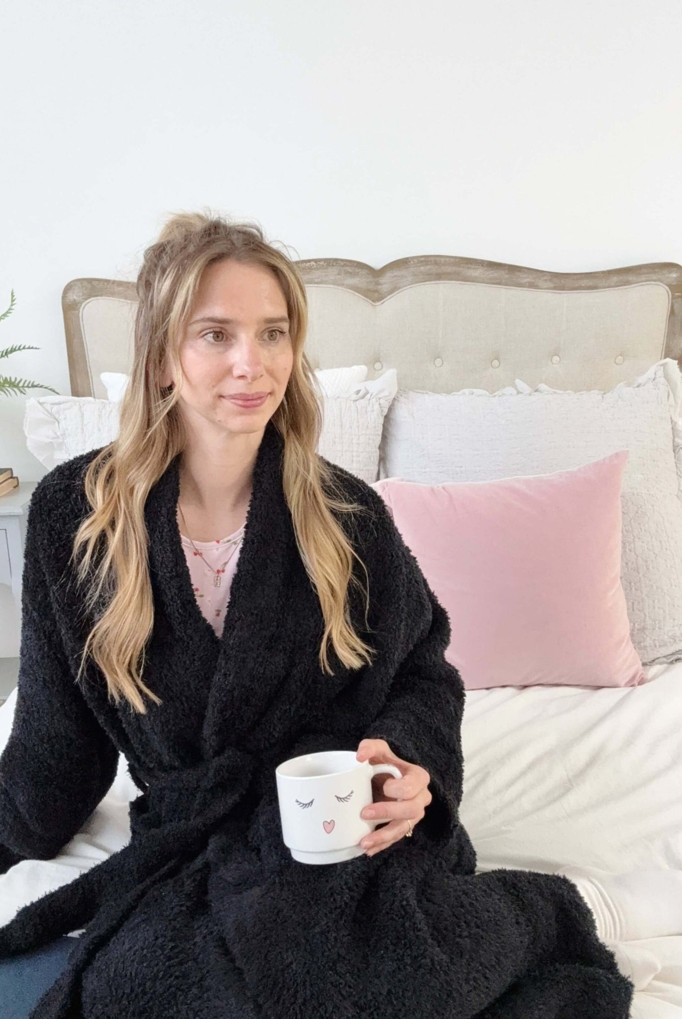 Black Chenille Cloud Spa Robe | Cozy Plush Lounge Woman in a black robe holding a mug on a bed with pink and gray pillows.