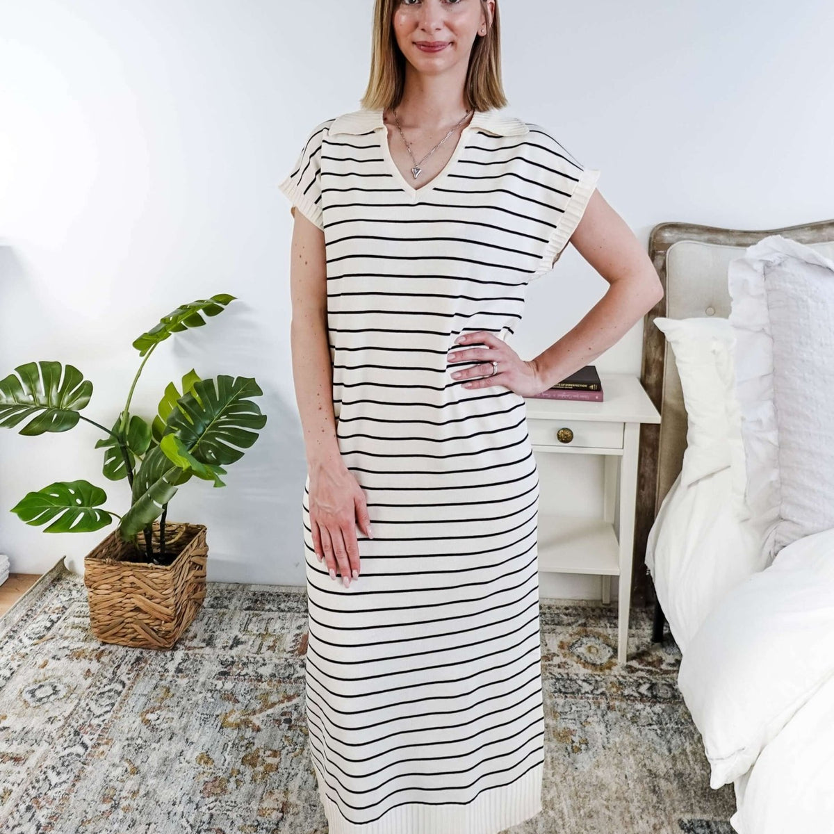 Woman wearing a black and white striped dress in a room with a plant and bed.