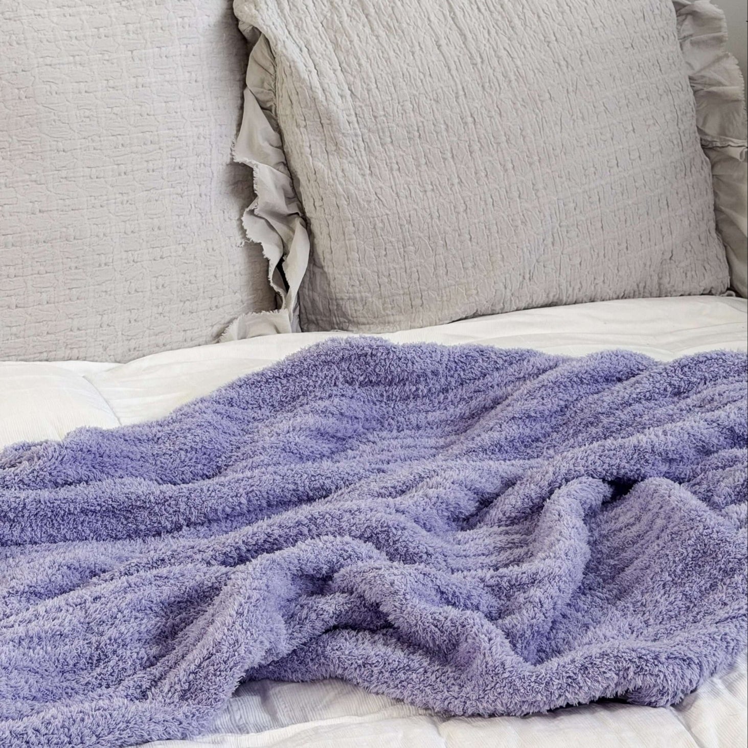 Lavender plush blanket Lounge by Jan Marie Bed with gray pillows and a purple blanket on a white background
