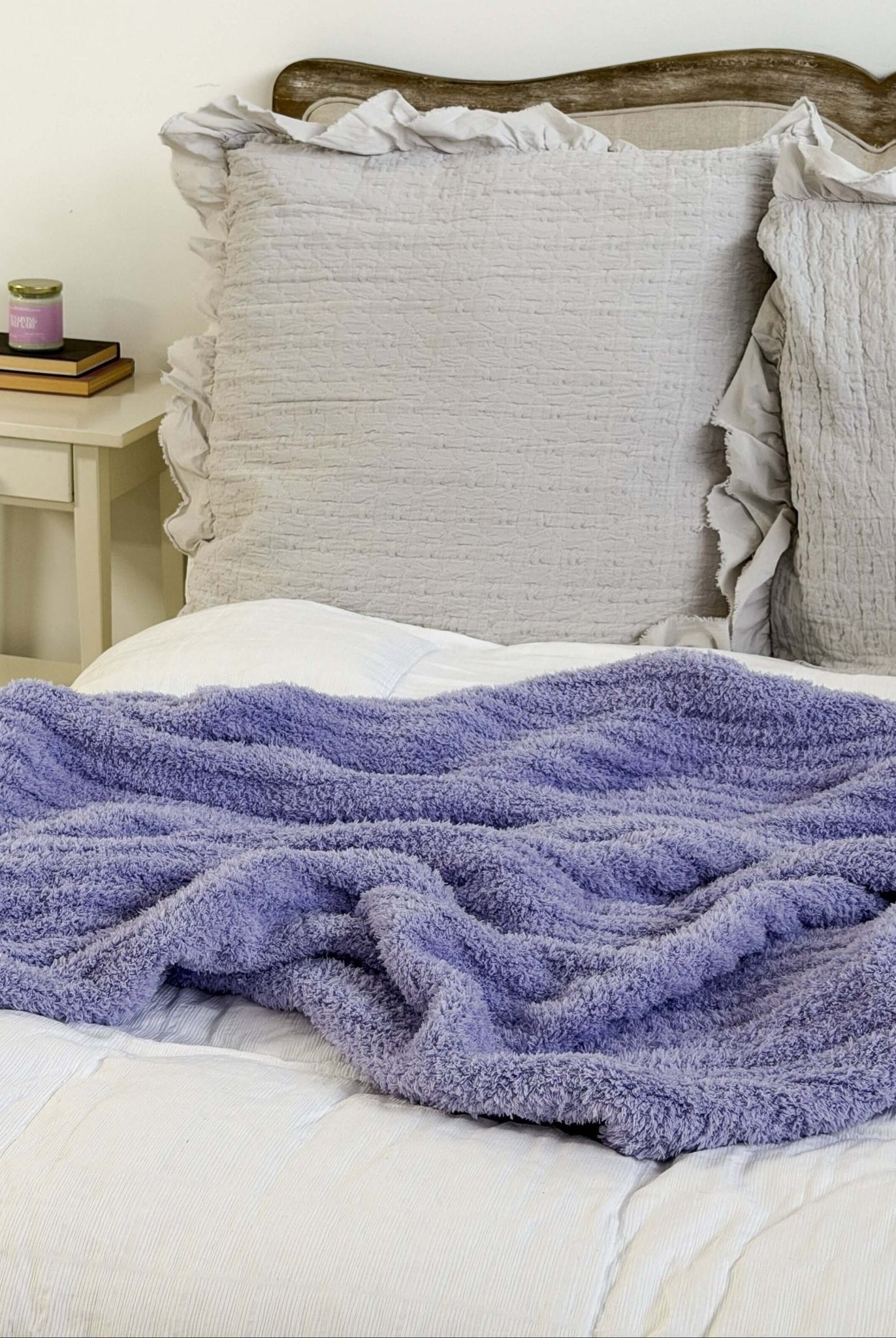 lavender plush cozy cabin blanket lounge by jan marie Bed with a purple blanket and gray pillows against a white wall.
