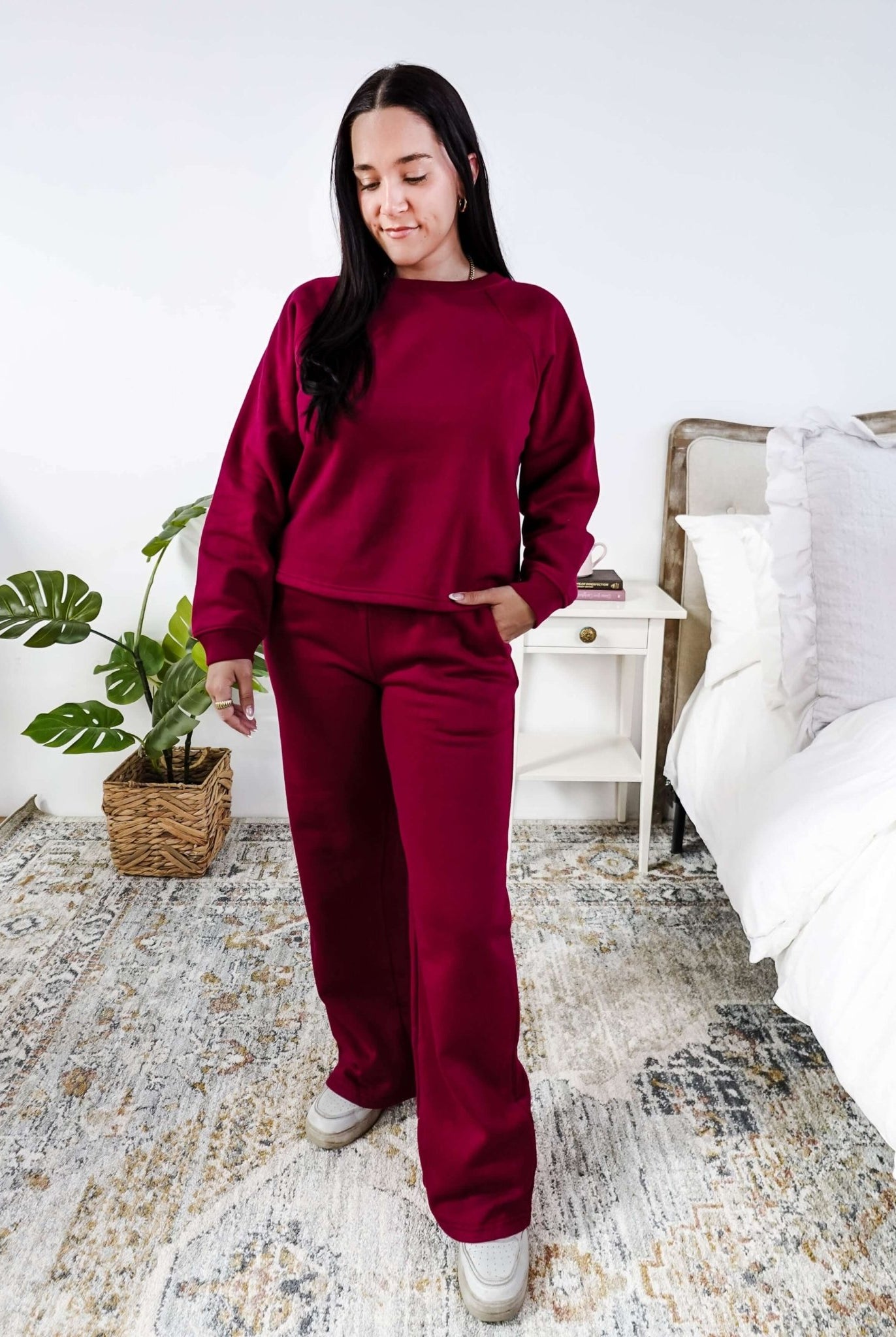 Woman wearing a red lounge outfit standing in a bedroom.