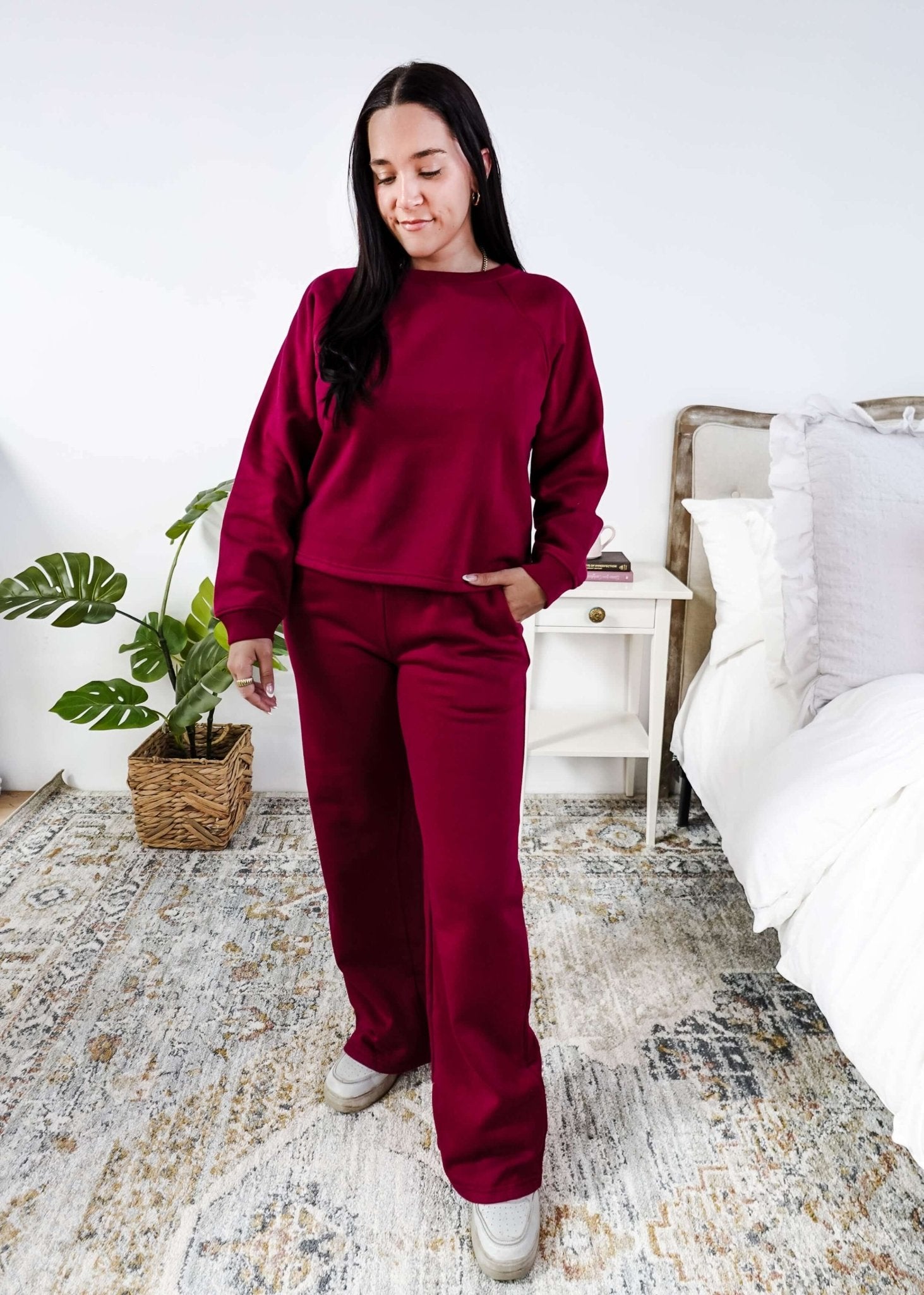Woman wearing a red lounge outfit standing in a bedroom.