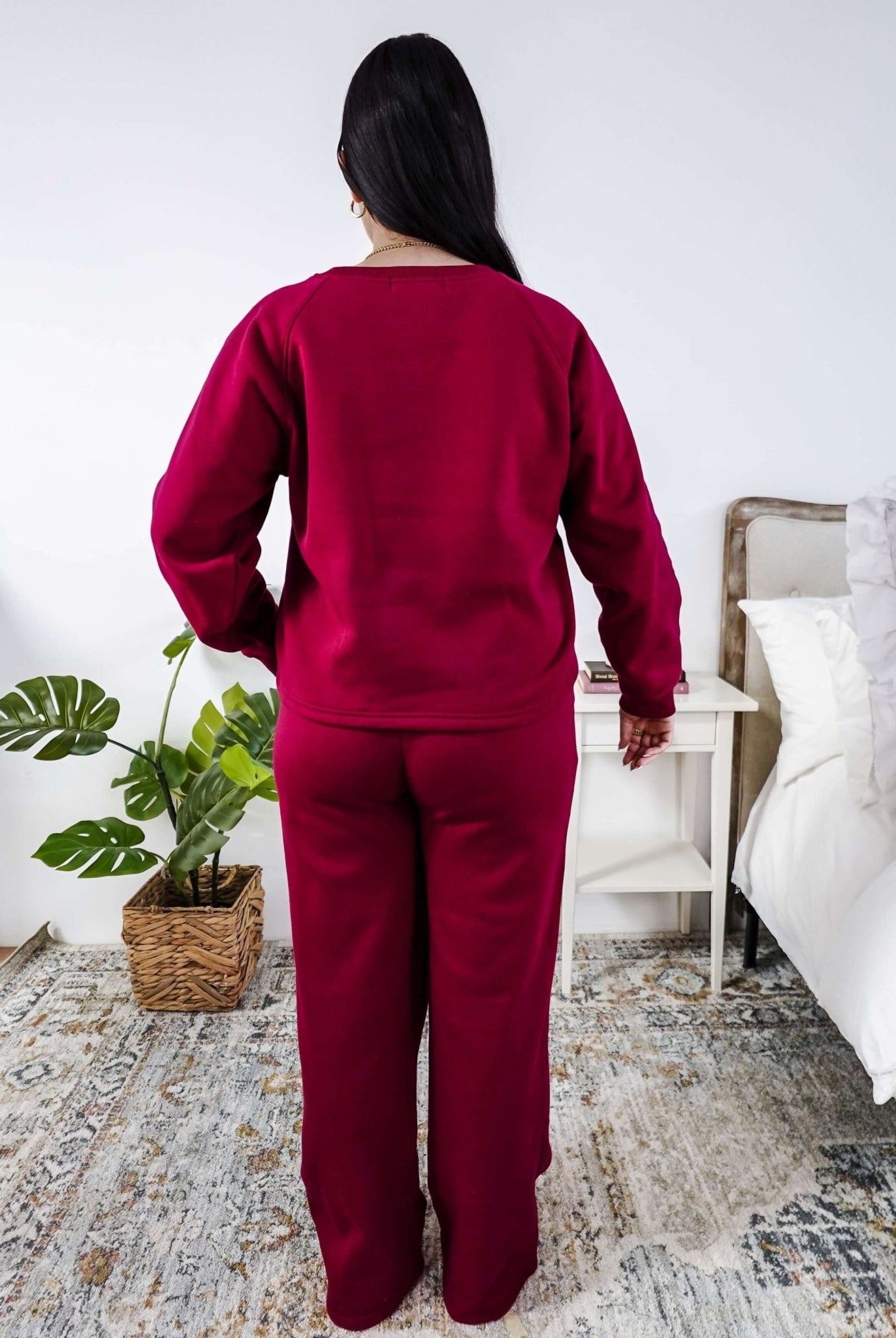 Woman wearing a red lounge outfit standing in a bedroom.