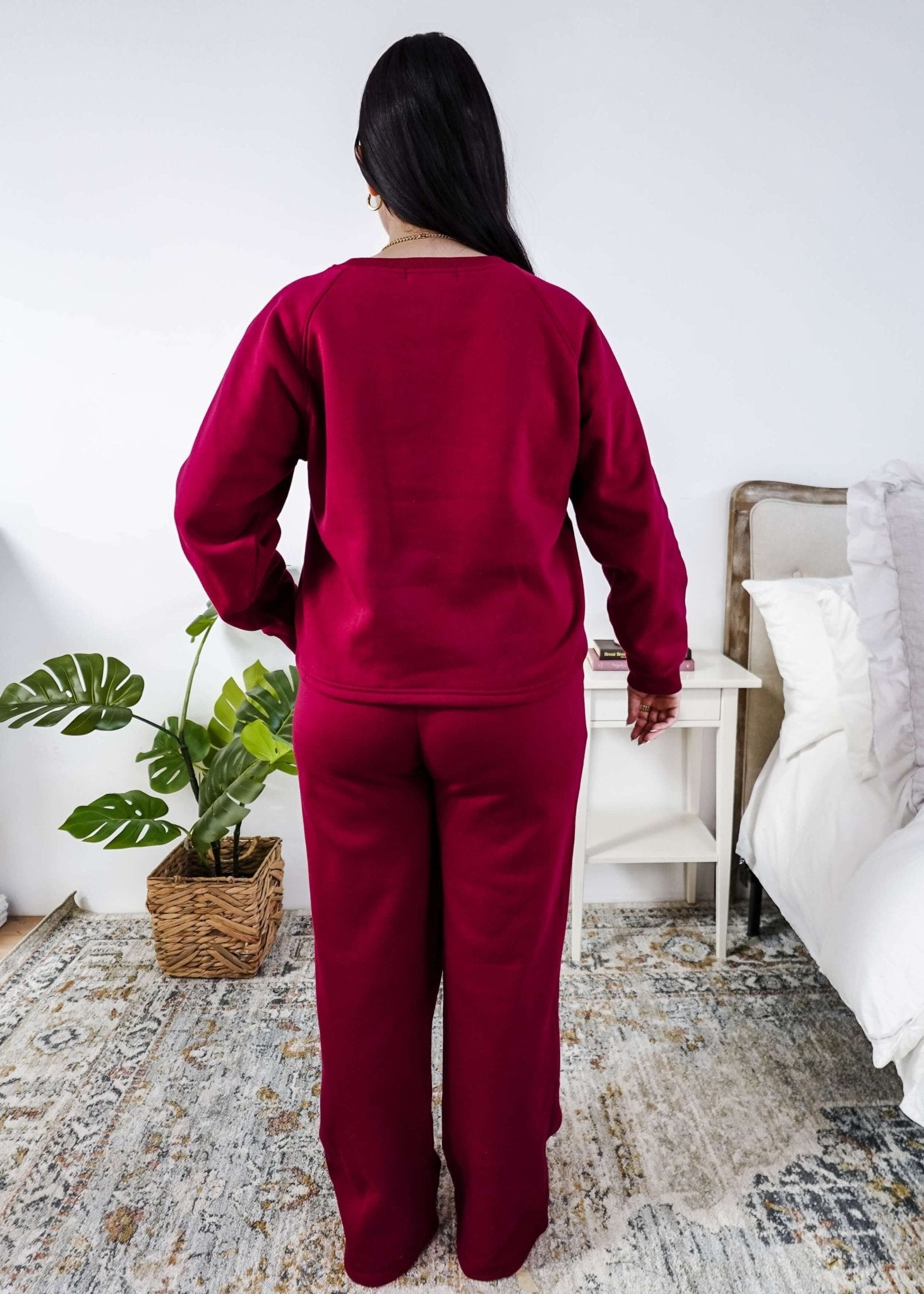 Woman wearing a red lounge outfit standing in a bedroom.