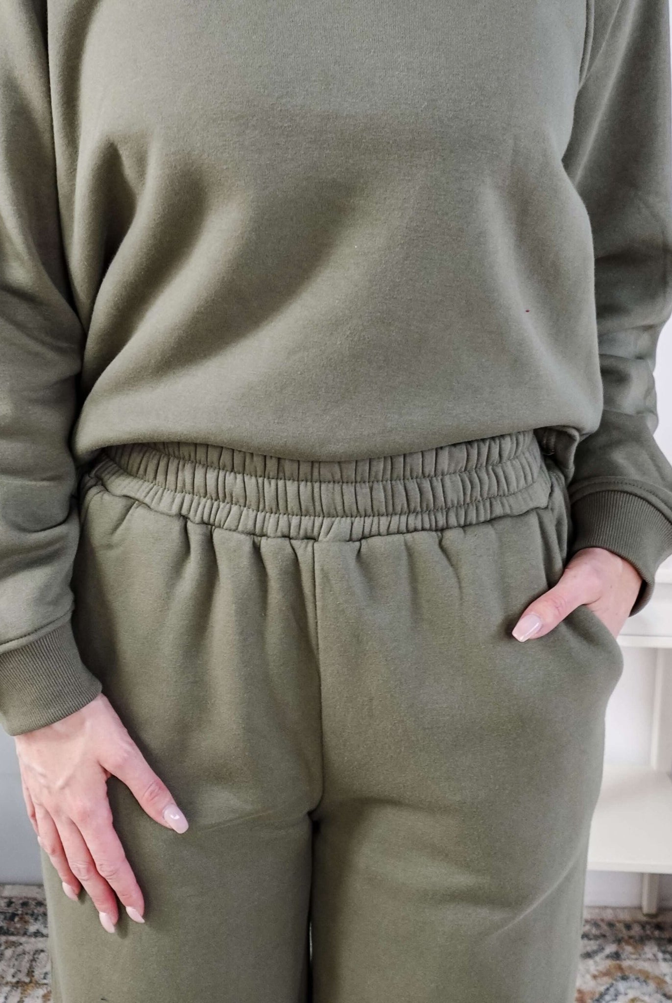 Person wearing a green sweatsuit with hands in pockets indoors.